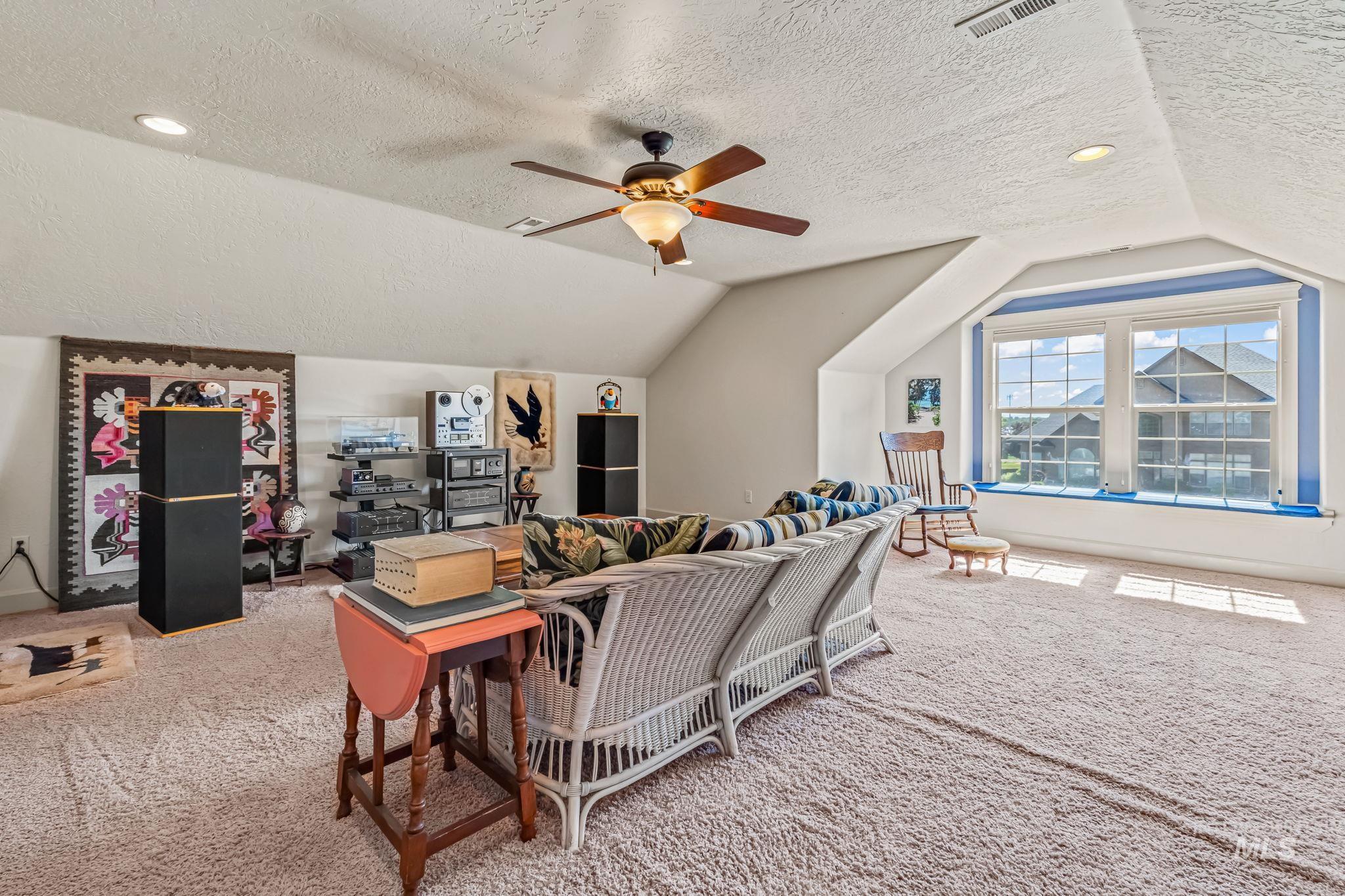 Carpeted living room with a textured ceiling, vaulted ceiling, and a ceiling fan