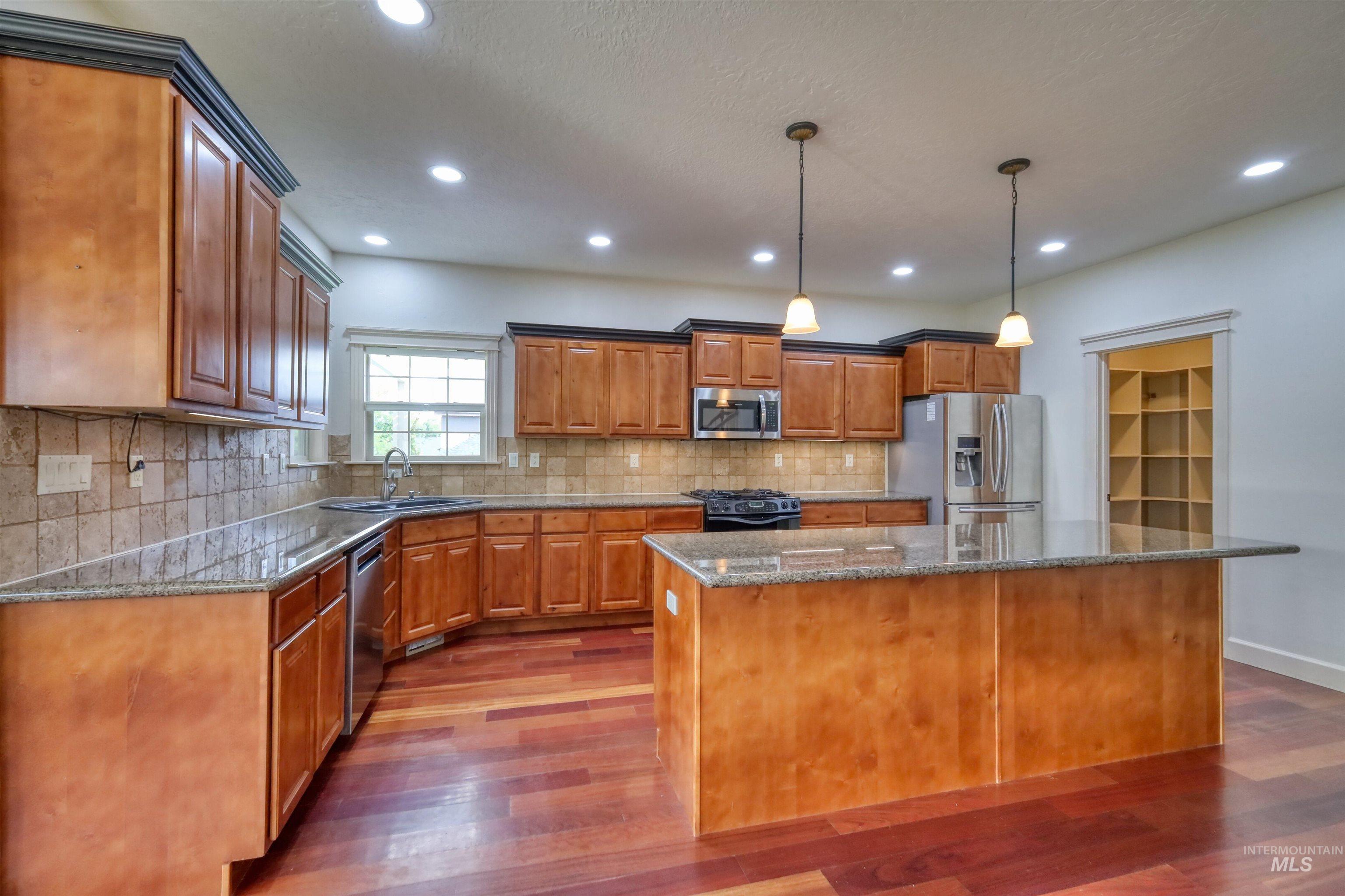 Kitchen featuring brown cabinets, dark stone countertops, appliances with stainless steel finishes, a center island, and tasteful backsplash