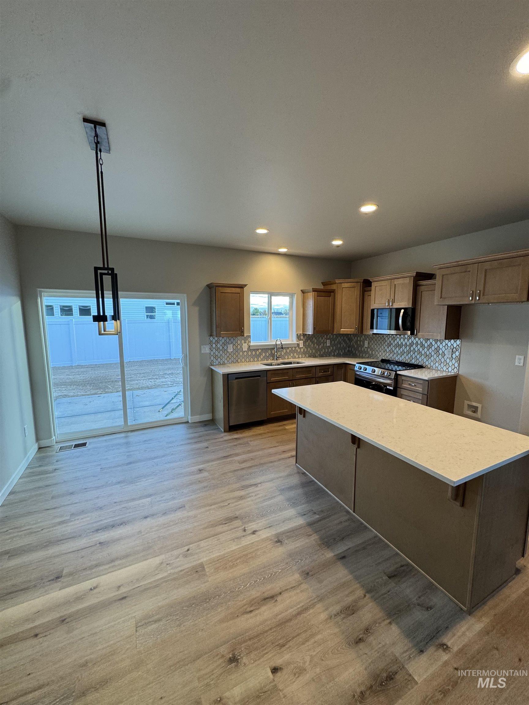 Kitchen with backsplash, decorative light fixtures, light wood-style floors, a kitchen island, and recessed lighting