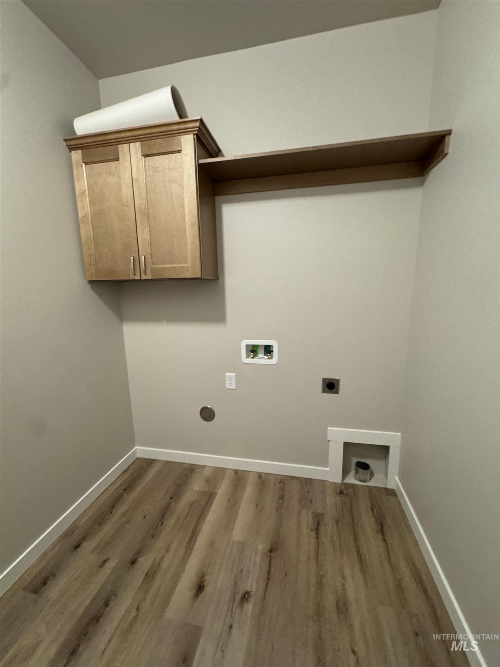 Washroom with hookup for an electric dryer, washer hookup, dark wood finished floors, and cabinet space