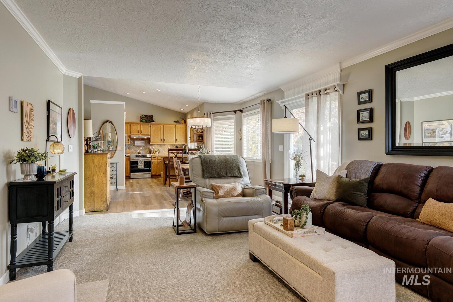 Living room with a textured ceiling, lofted ceiling, crown molding, and light carpet