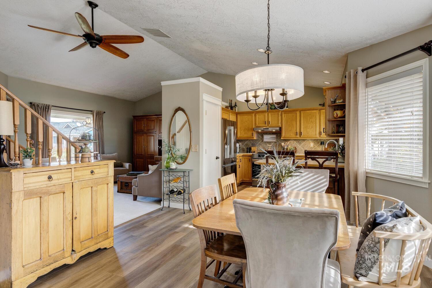 Dining space featuring vaulted ceiling, light wood finished floors, a ceiling fan, stairs, and a textured ceiling