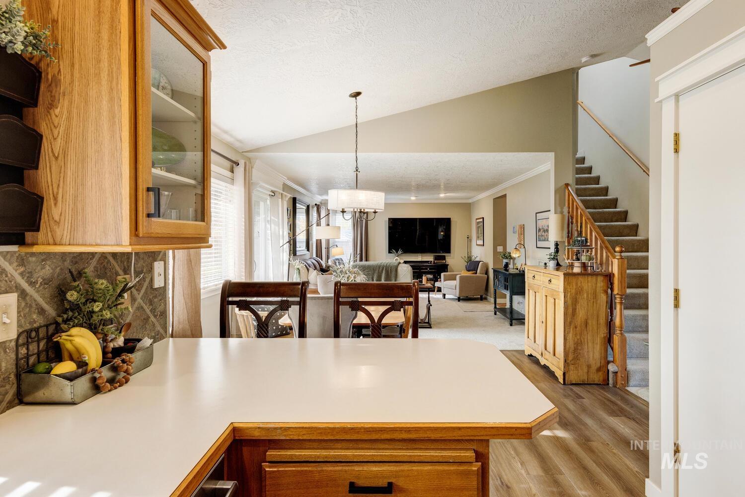 Kitchen with light countertops, vaulted ceiling, a textured ceiling, ornamental molding, and pendant lighting