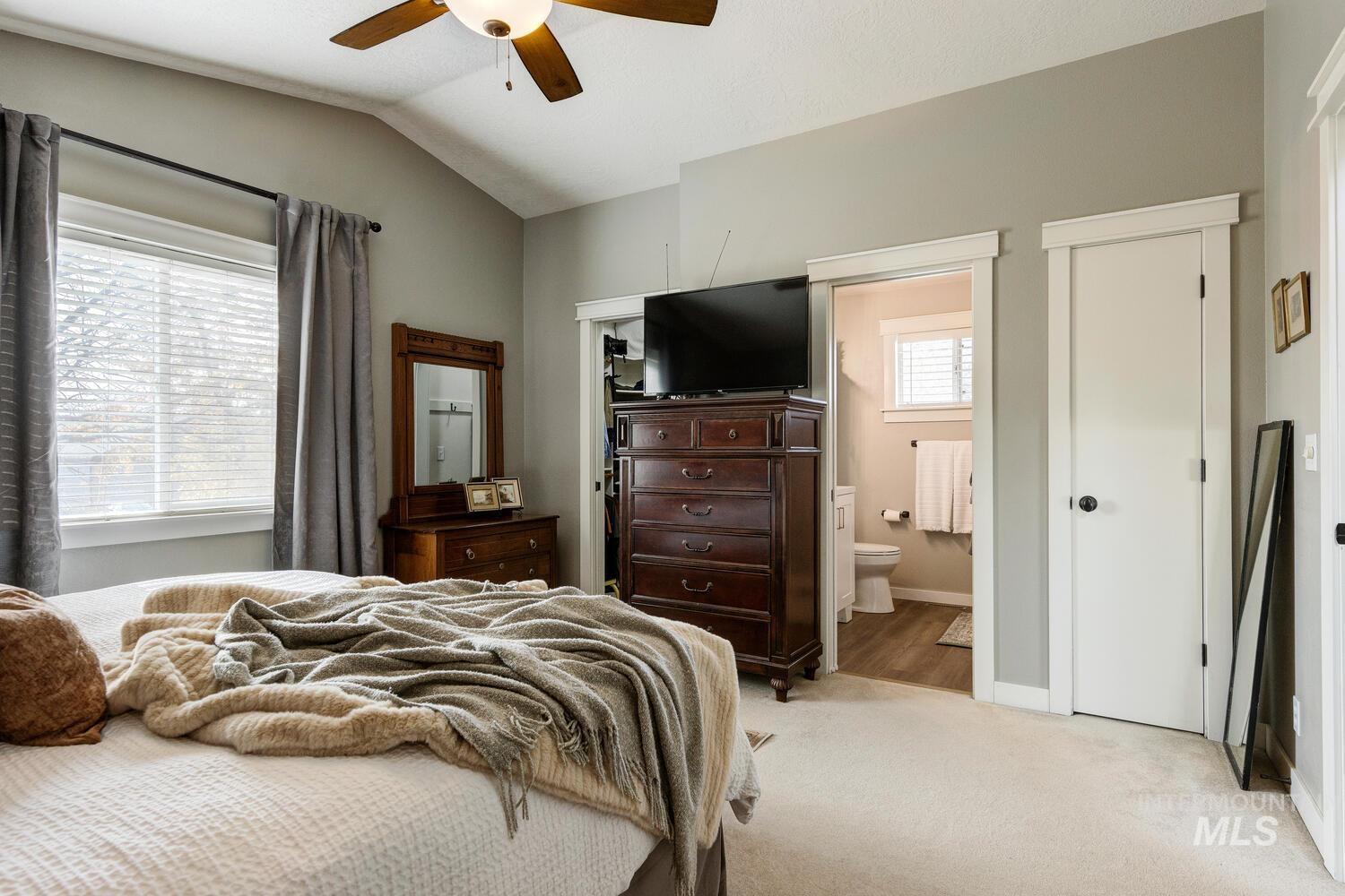 Carpeted bedroom featuring a closet, lofted ceiling, ceiling fan, and ensuite bathroom