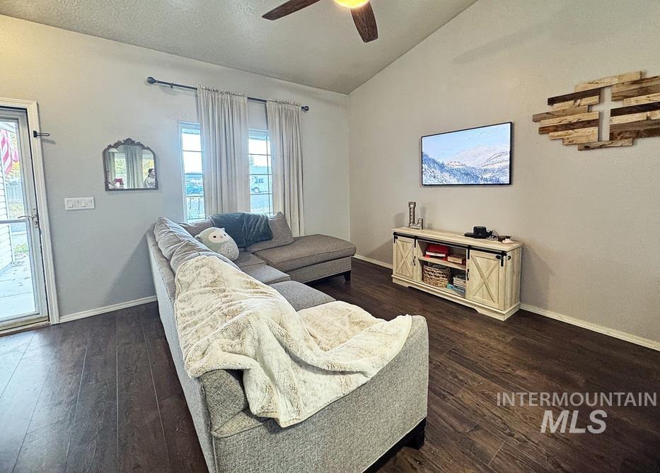 Living area featuring lofted ceiling, dark wood-style flooring, a ceiling fan, and a textured ceiling