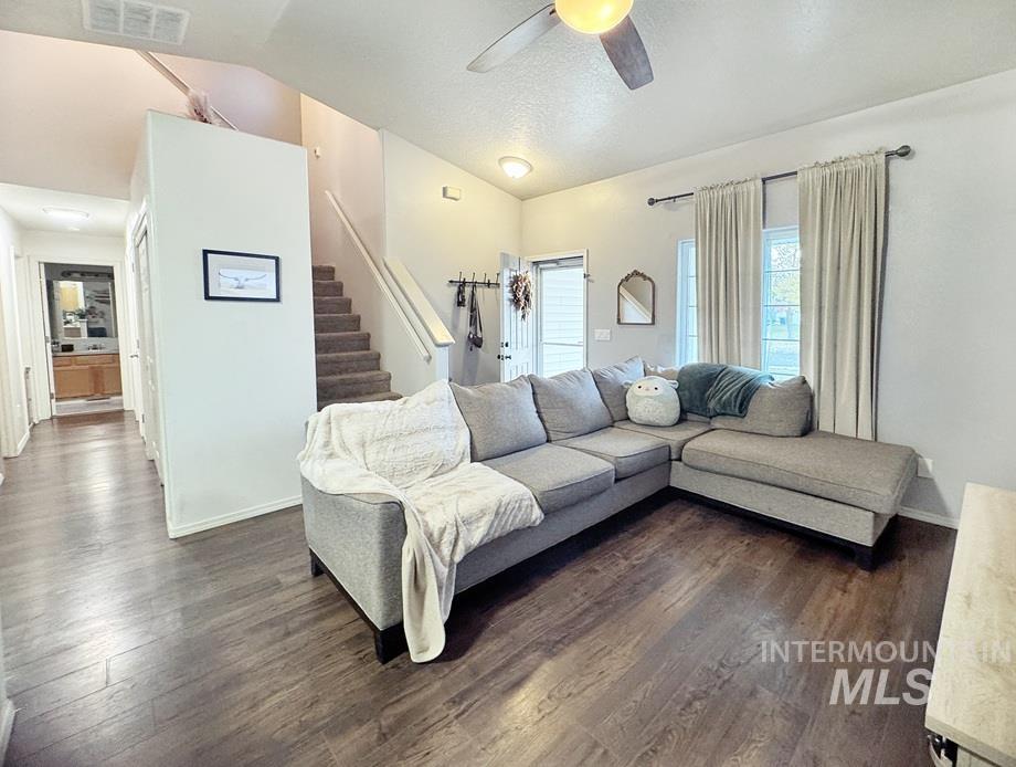 Living room with dark wood finished floors, vaulted ceiling, stairs, a ceiling fan, and a textured ceiling