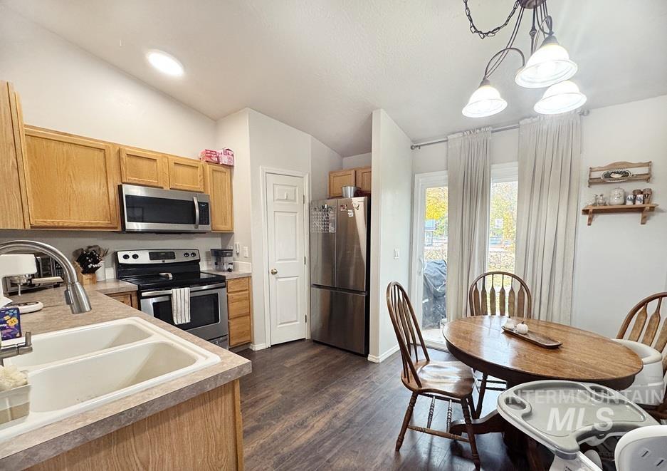 Kitchen with stainless steel appliances, decorative light fixtures, lofted ceiling, dark wood-type flooring, and light countertops