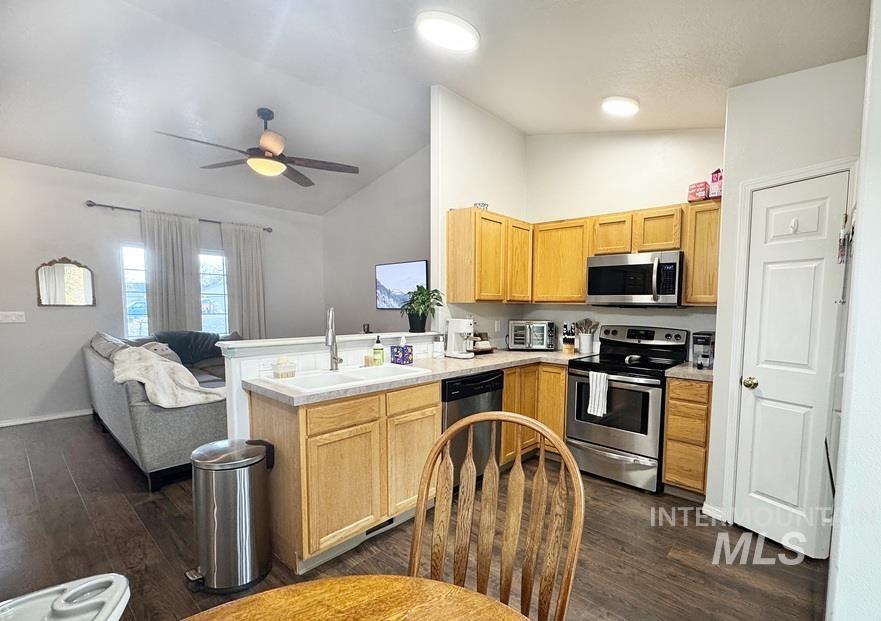 Kitchen with vaulted ceiling, open floor plan, stainless steel appliances, a peninsula, and dark wood finished floors