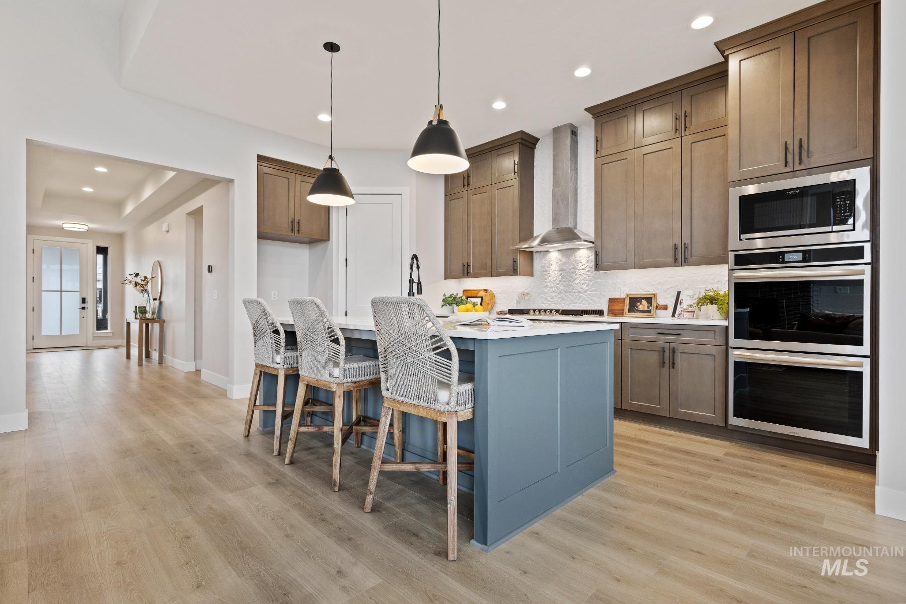Kitchen featuring decorative light fixtures, decorative backsplash, appliances with stainless steel finishes, a kitchen bar, and a kitchen island with sink