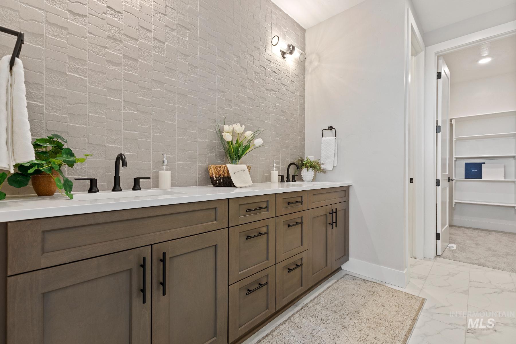 Full bath with double vanity, a spacious closet, and light marble finish flooring