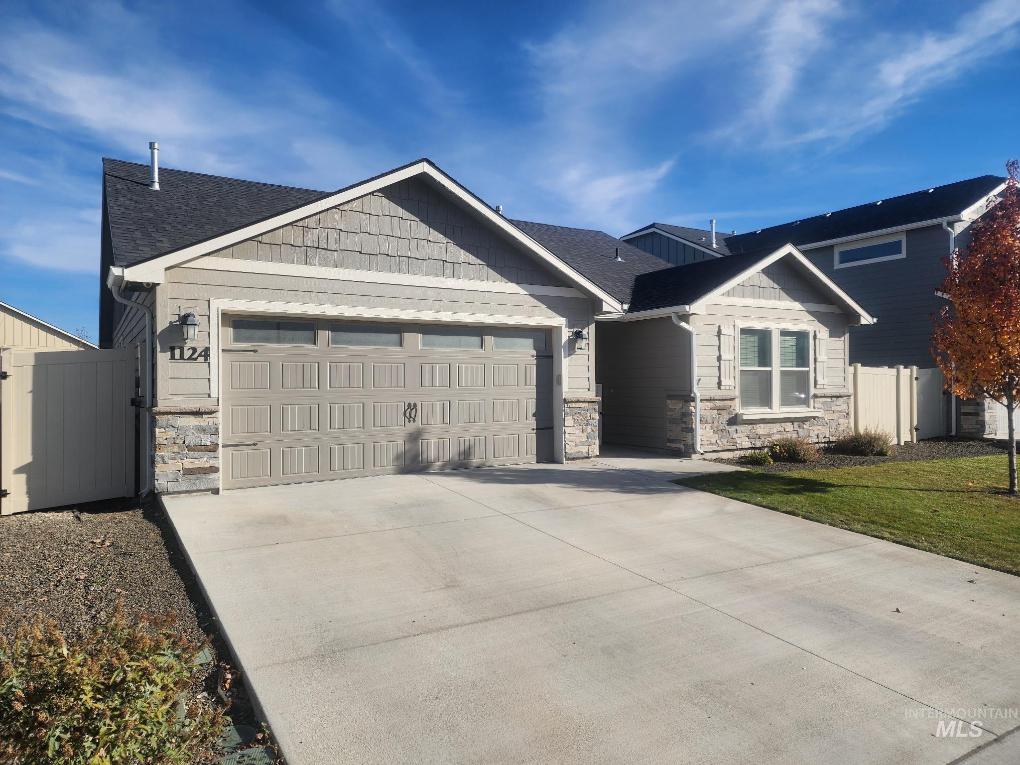 Craftsman-style home featuring stone siding, a shingled roof, concrete driveway, an attached garage, and a gate