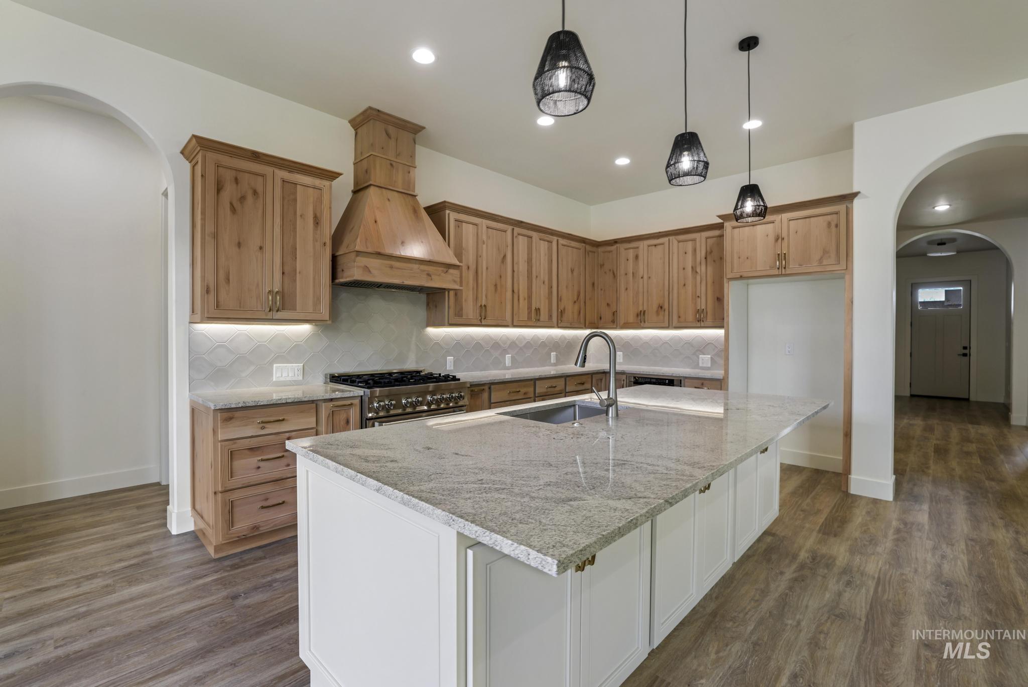 Kitchen featuring arched walkways, tasteful backsplash, light stone countertops, pendant lighting, and recessed lighting