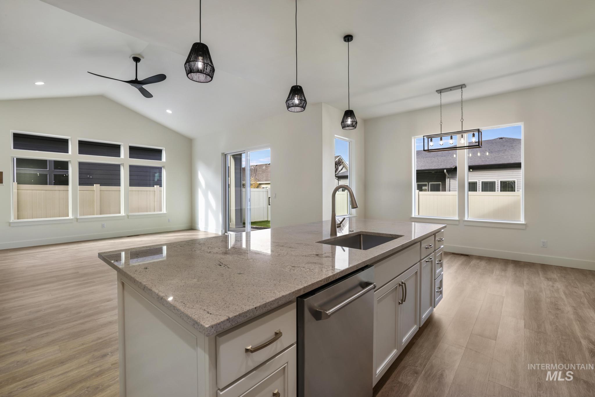 Kitchen with light stone countertops, lofted ceiling, light wood-style floors, stainless steel dishwasher, and hanging light fixtures