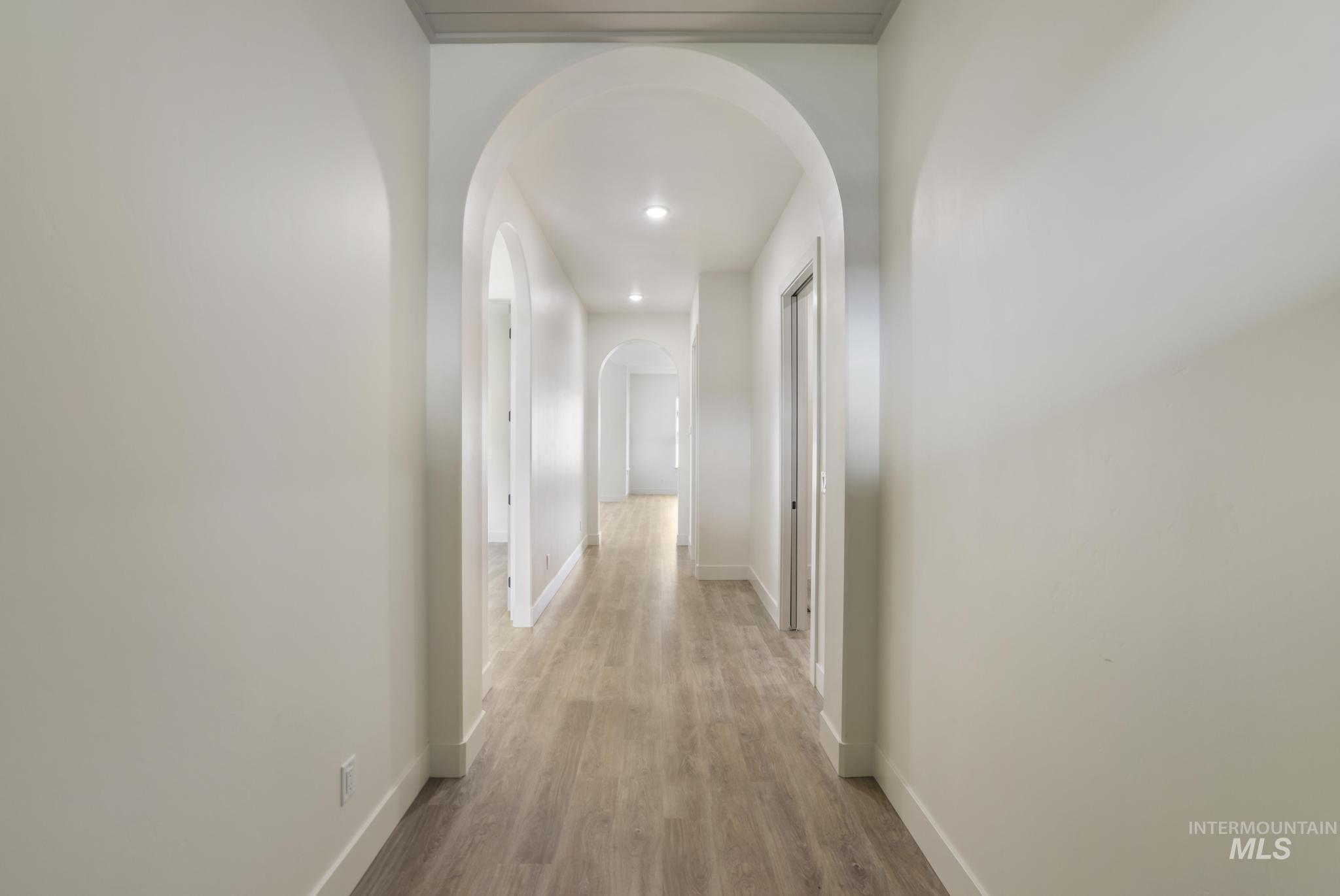 Corridor featuring arched walkways, light wood-type flooring, and recessed lighting