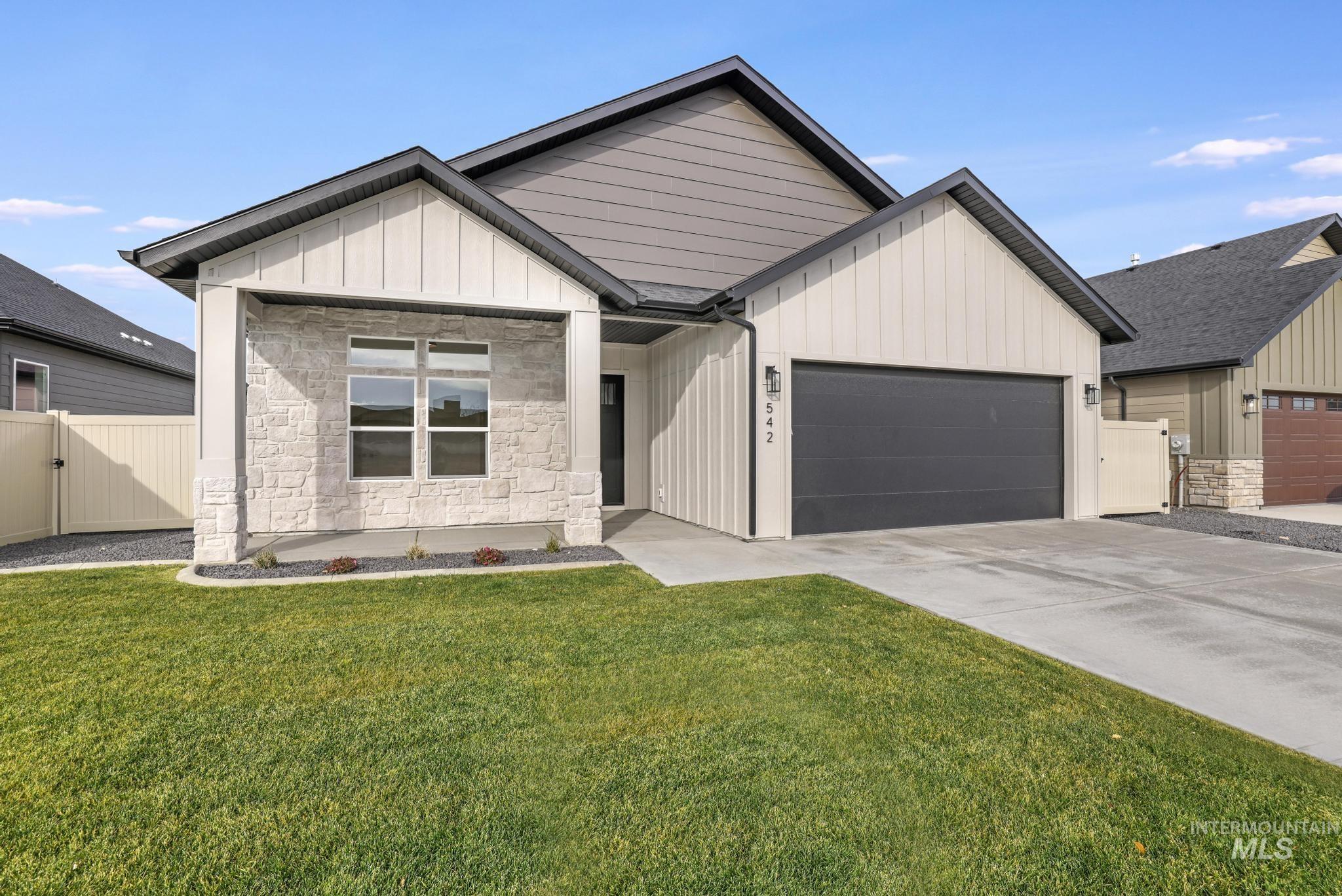 Modern farmhouse with board and batten siding, stone siding, a gate, concrete driveway, and a garage