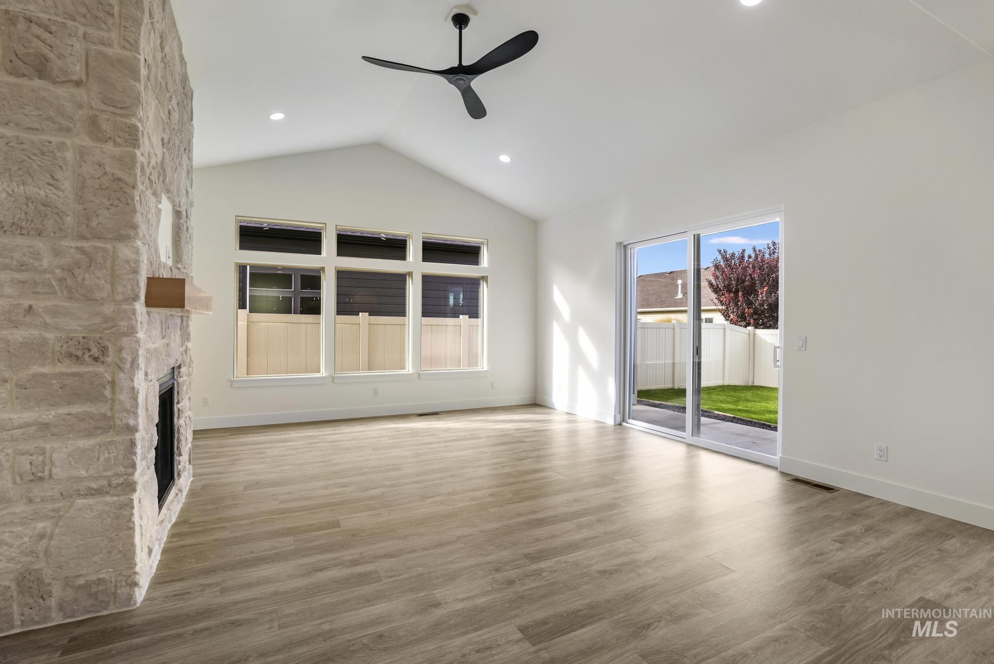 Unfurnished living room with light wood finished floors, ceiling fan, a fireplace, and high vaulted ceiling