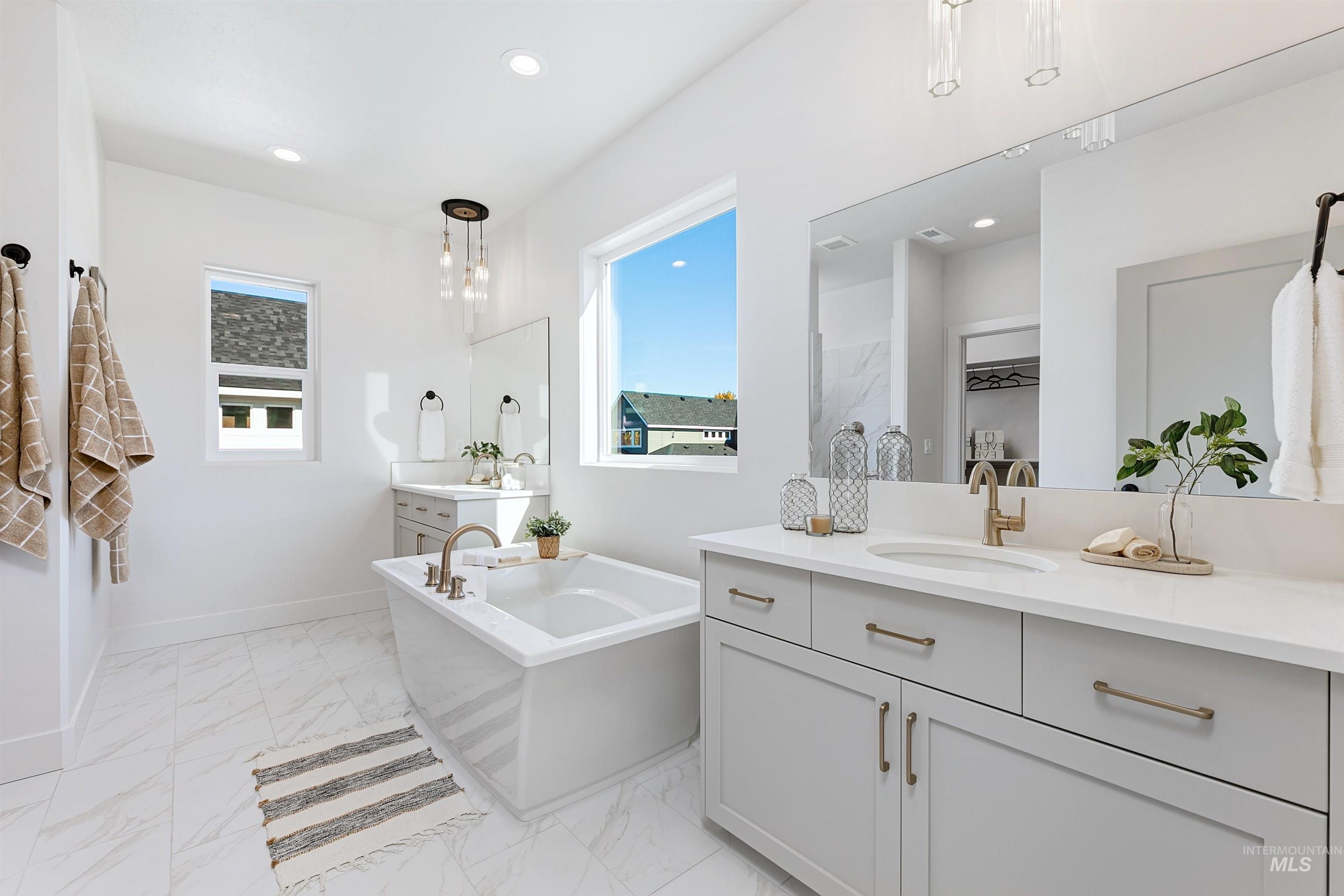 Full bath with two vanities, light marble finish floors, a soaking tub, and recessed lighting