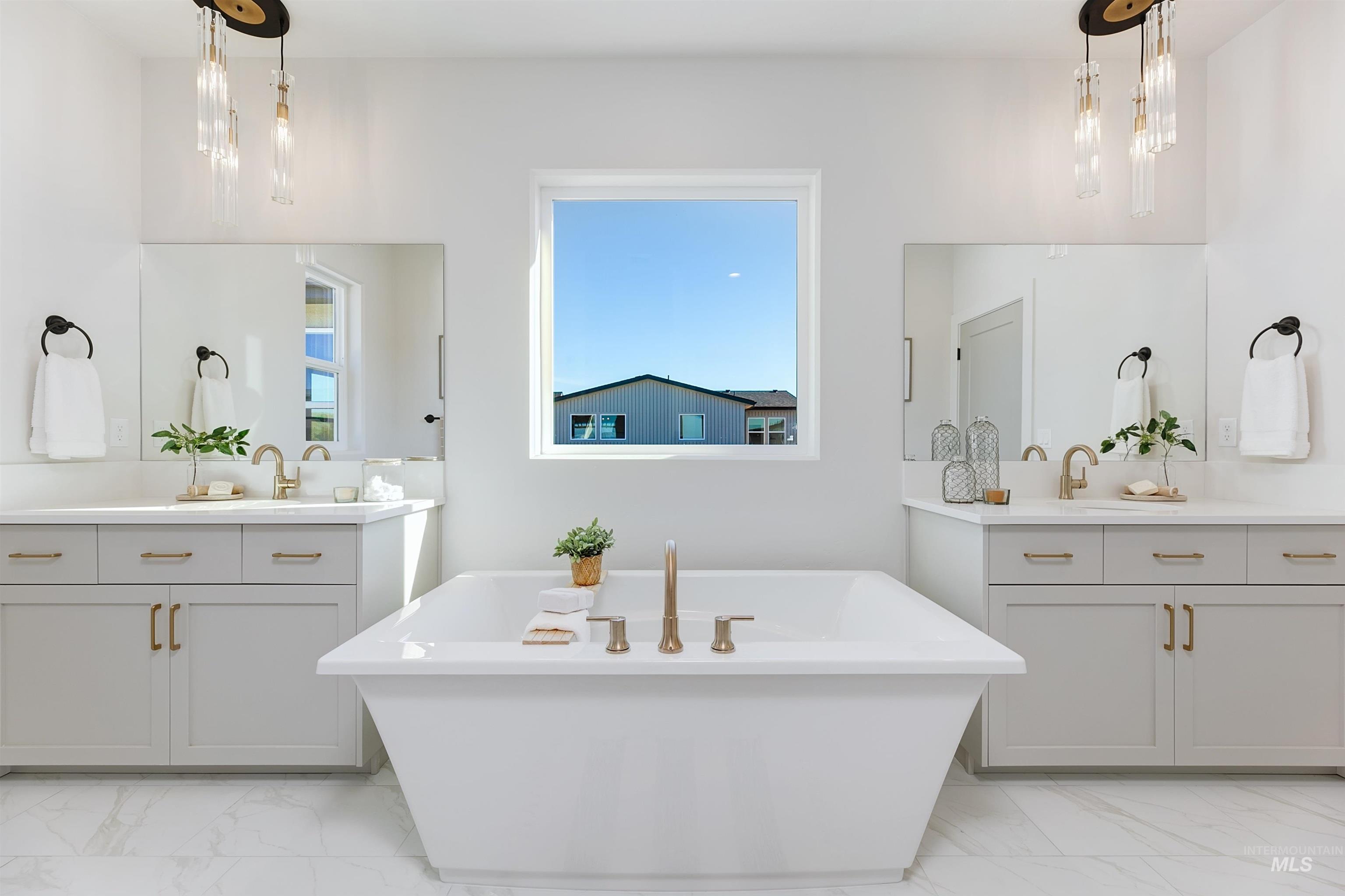 Full bathroom featuring light marble finish floors, a freestanding tub, and two vanities