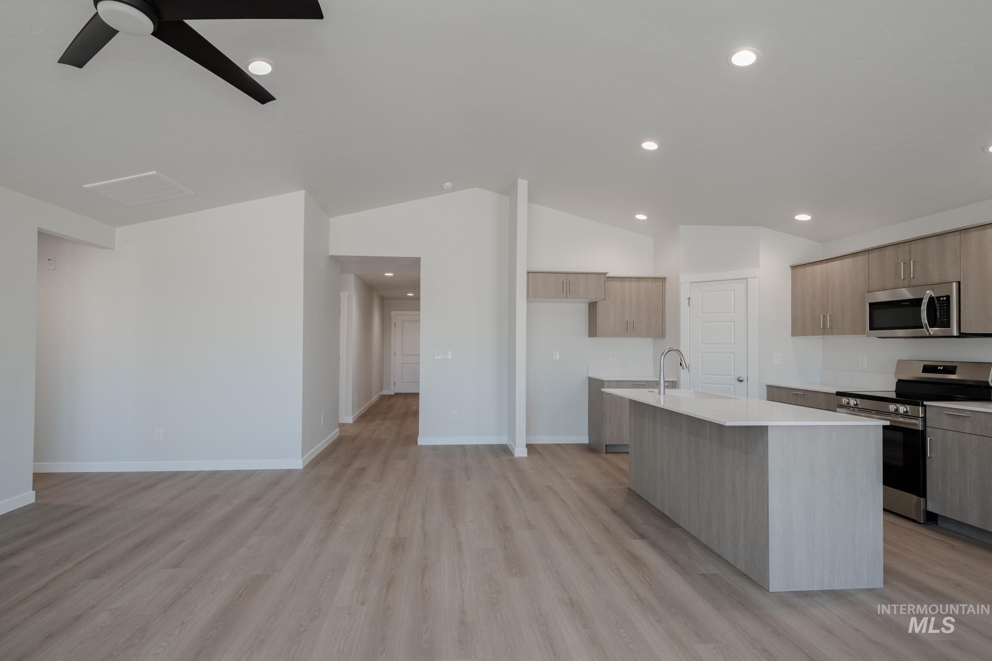 Kitchen featuring stainless steel appliances, light wood finished floors, lofted ceiling, a kitchen island with sink, and recessed lighting