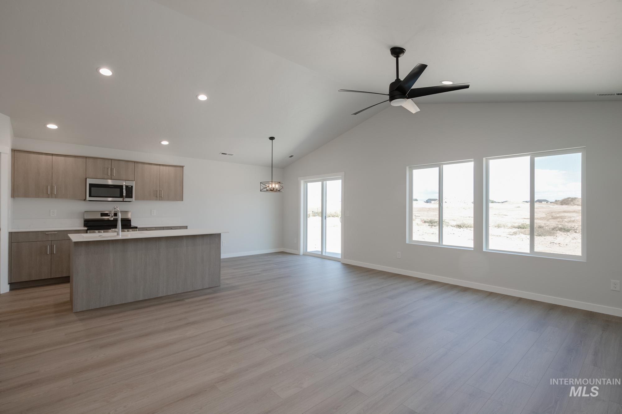 Kitchen featuring open floor plan, a kitchen island with sink, light wood finished floors, vaulted ceiling, and appliances with stainless steel finishes