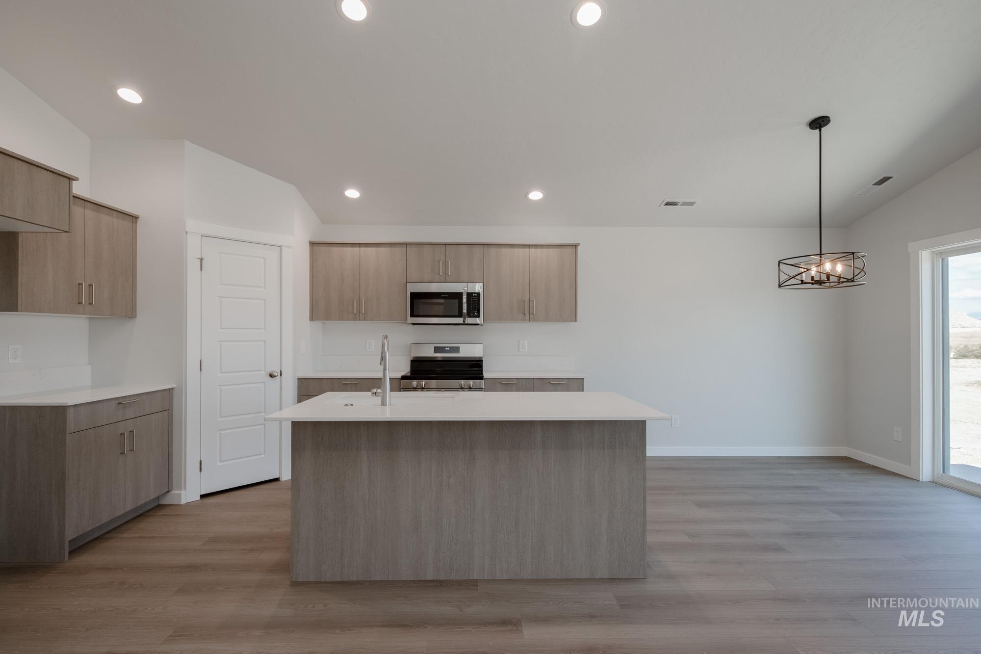 Kitchen featuring stainless steel appliances, recessed lighting, decorative light fixtures, light wood finished floors, and an island with sink