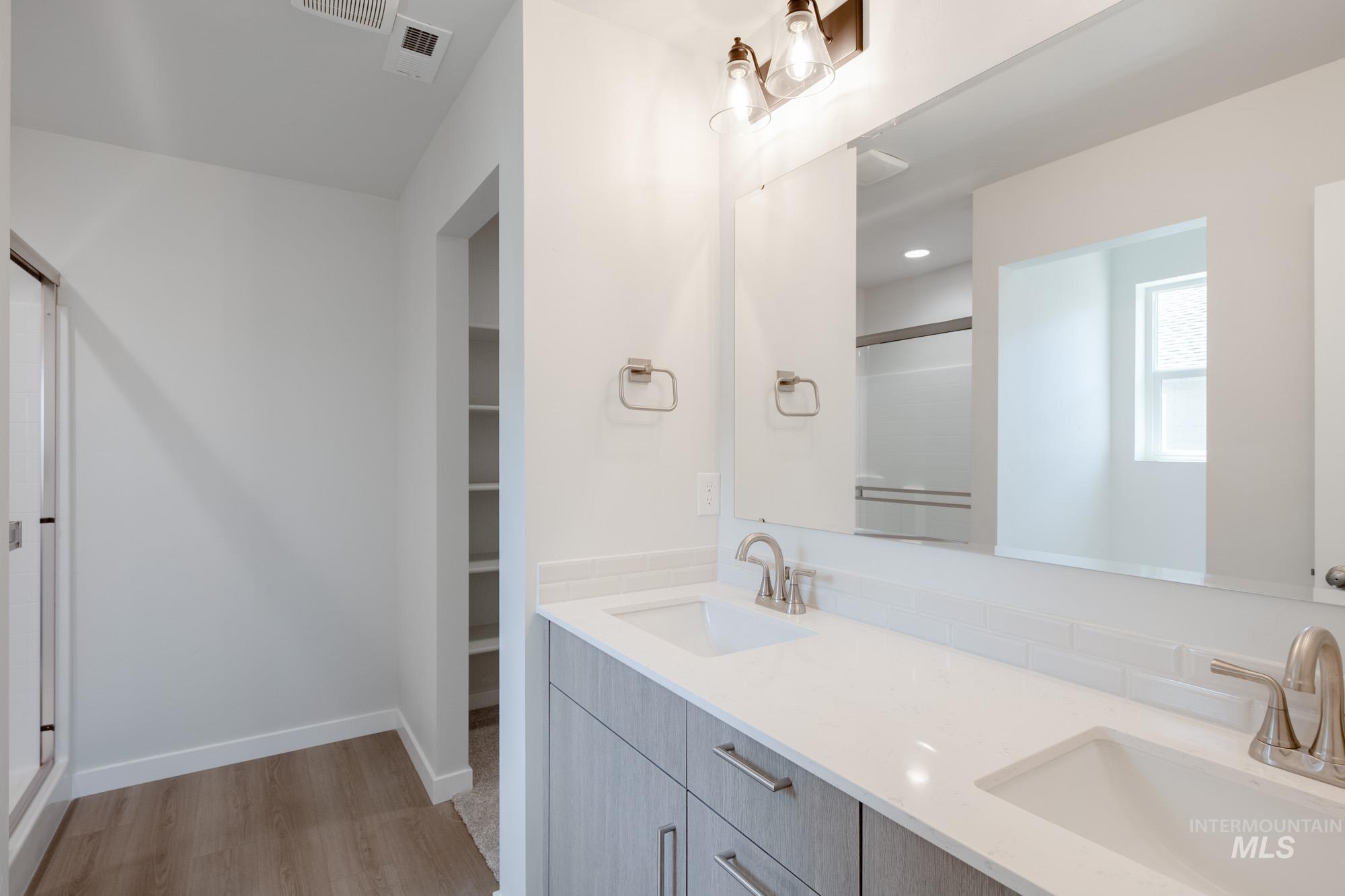 Full bath featuring a shower stall, double vanity, light wood finished floors, and a walk in closet