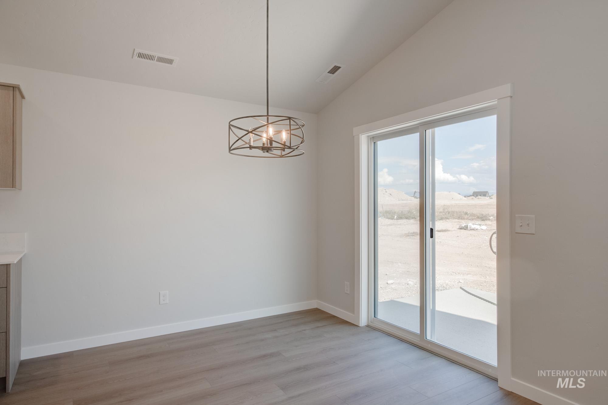 Unfurnished dining area featuring vaulted ceiling, a chandelier, and light wood finished floors