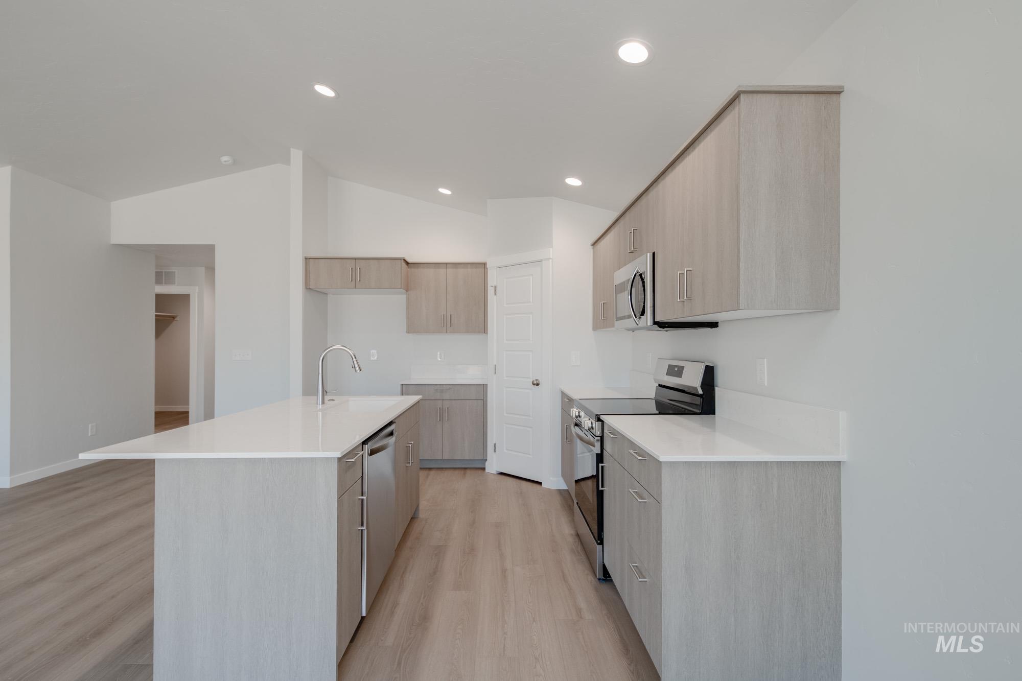 Kitchen with modern cabinets, light brown cabinetry, stainless steel appliances, light wood-type flooring, and a center island with sink