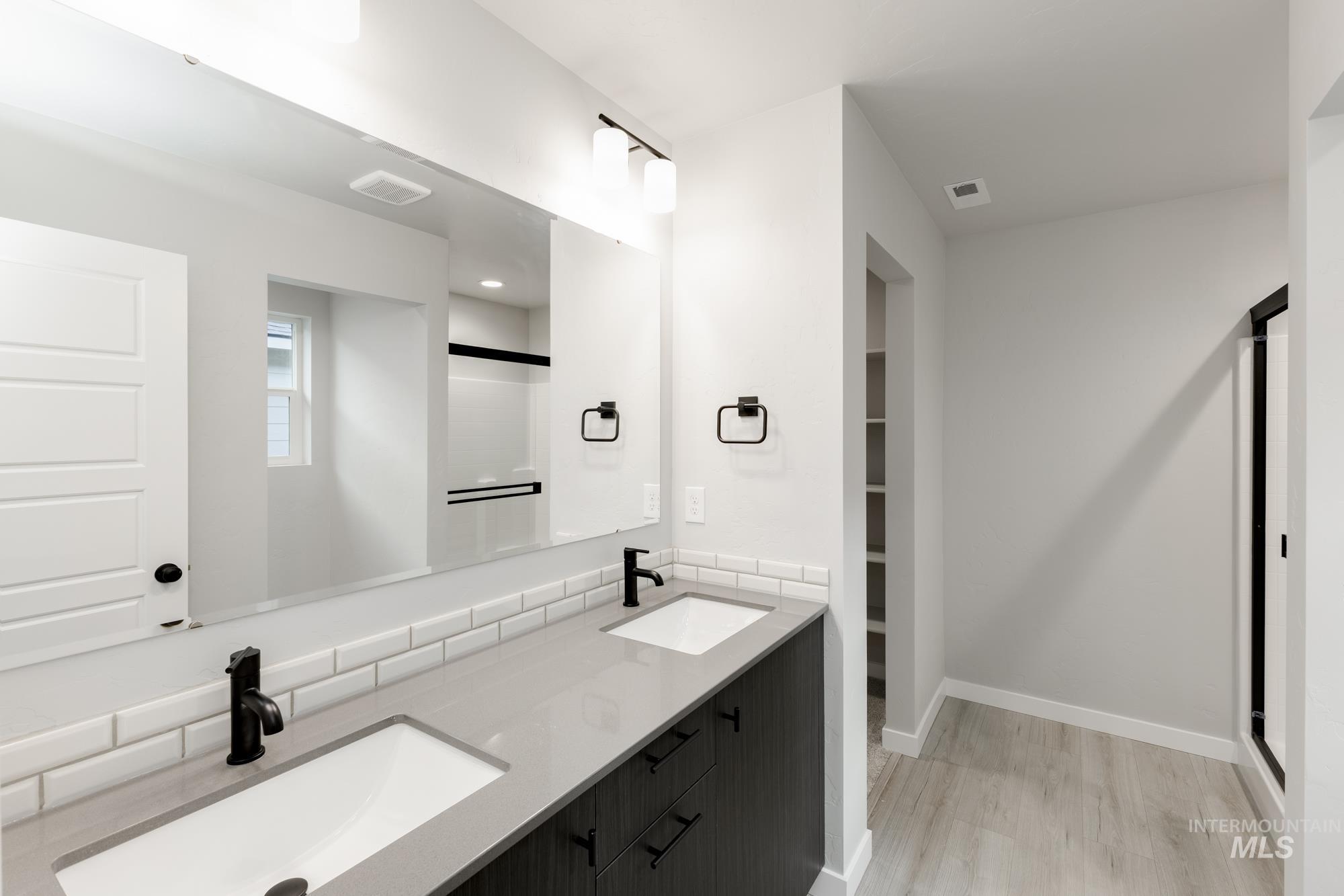 Bathroom featuring double vanity, a shower stall, a walk in closet, and light wood-style floors