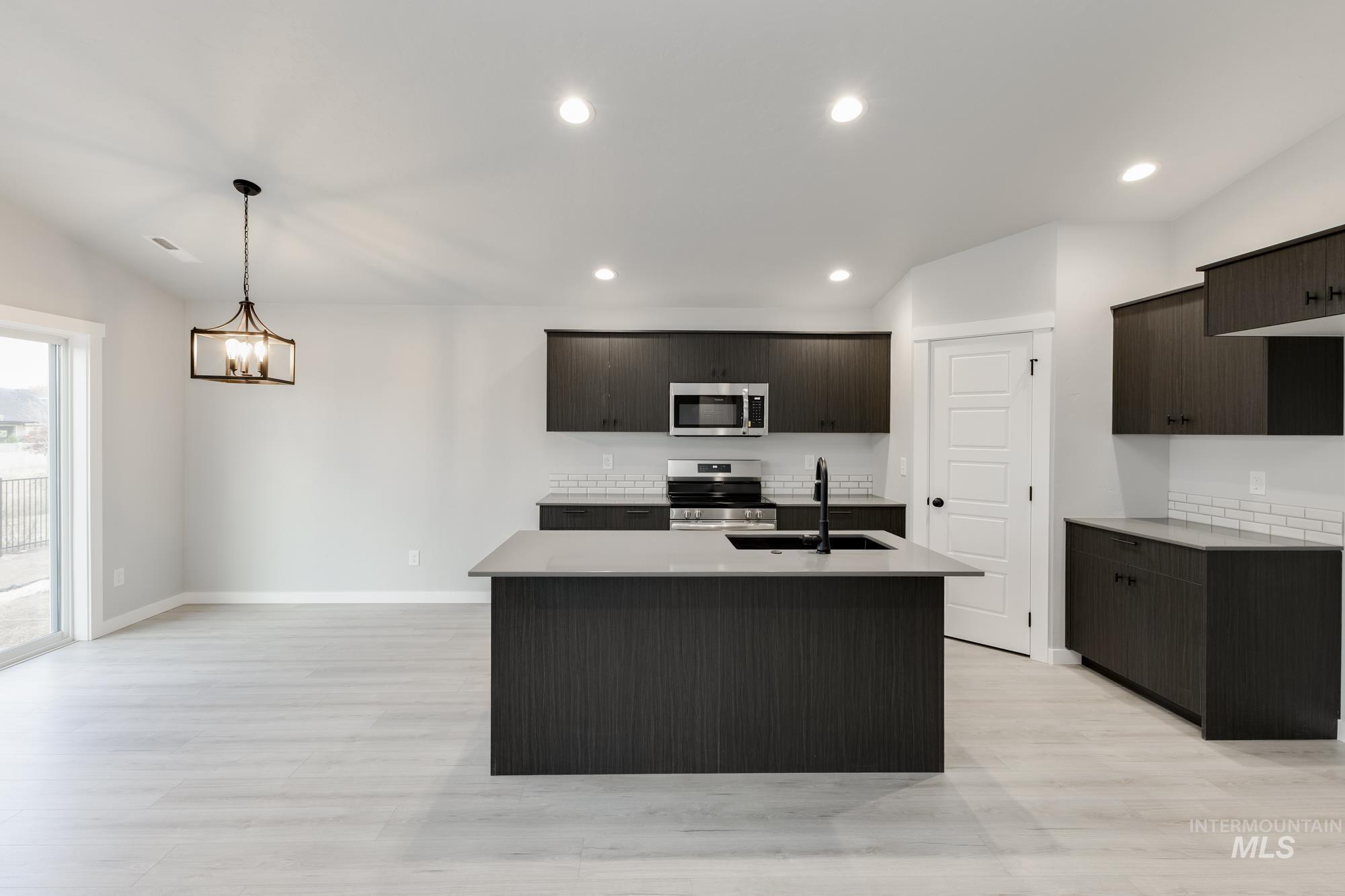 Kitchen featuring stainless steel appliances, an island with sink, recessed lighting, light wood-style flooring, and hanging light fixtures