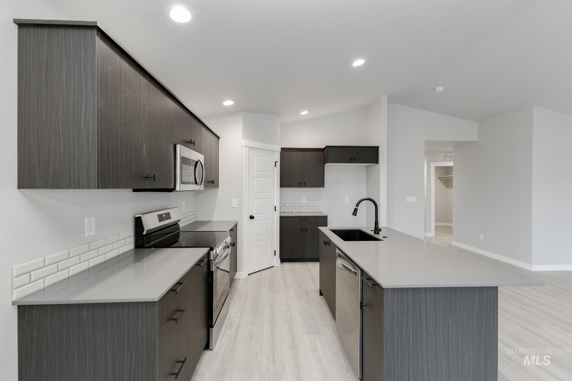 Kitchen with appliances with stainless steel finishes, light wood-type flooring, vaulted ceiling, modern cabinets, and a center island with sink