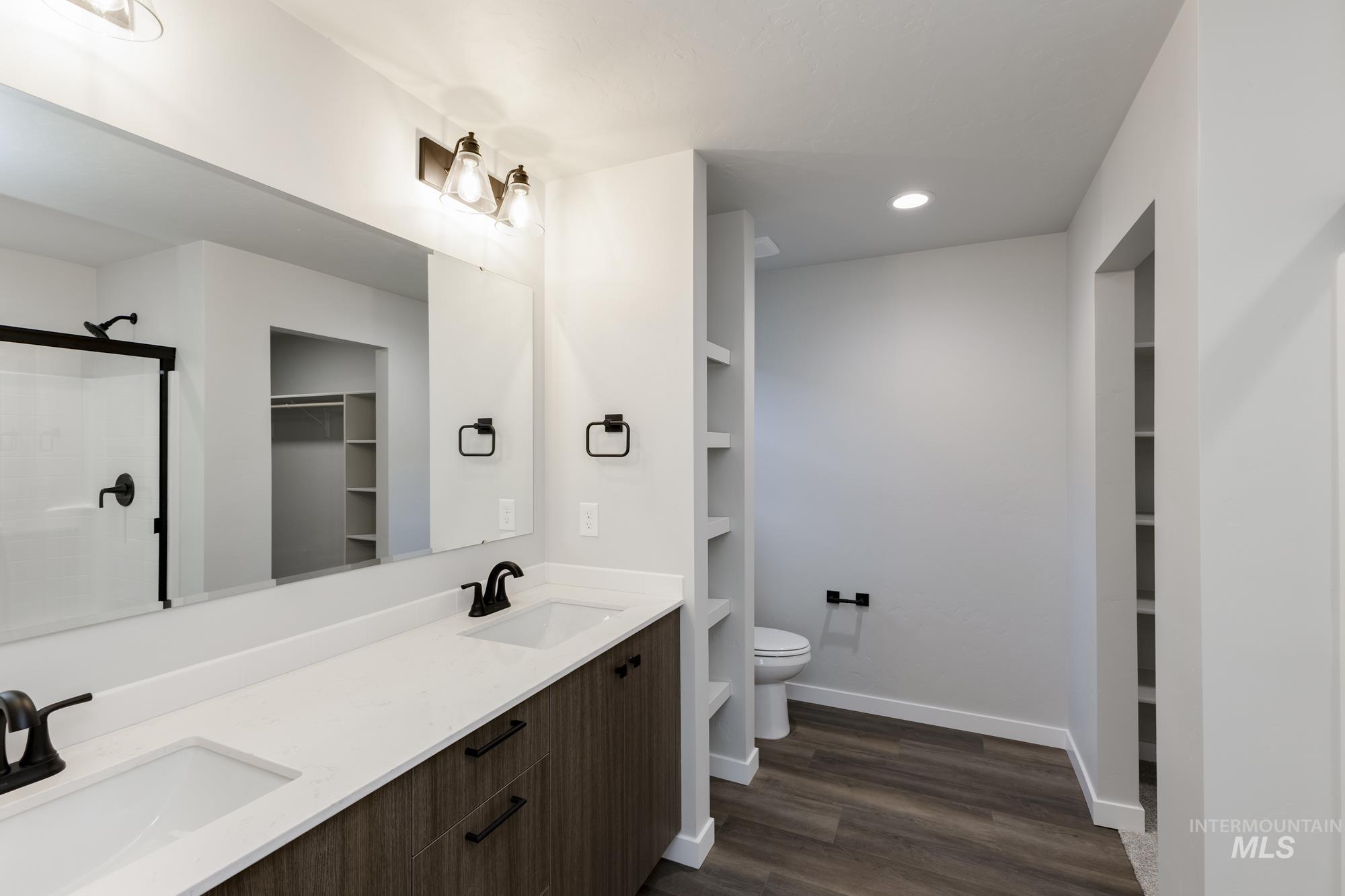 Bathroom with a walk in closet, double vanity, dark wood-style flooring, recessed lighting, and a shower stall