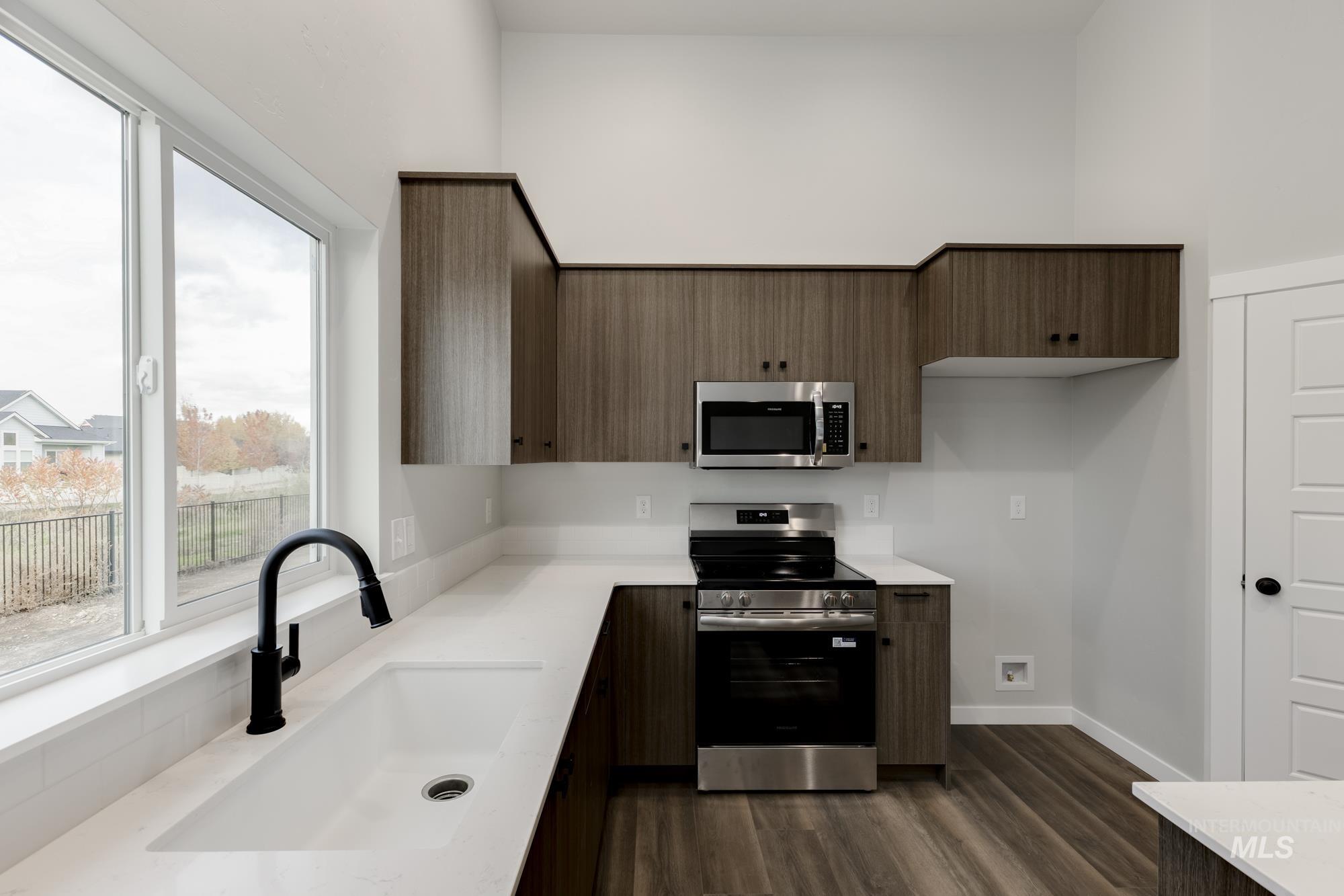 Kitchen with appliances with stainless steel finishes, dark wood finished floors, modern cabinets, dark brown cabinets, and light stone countertops
