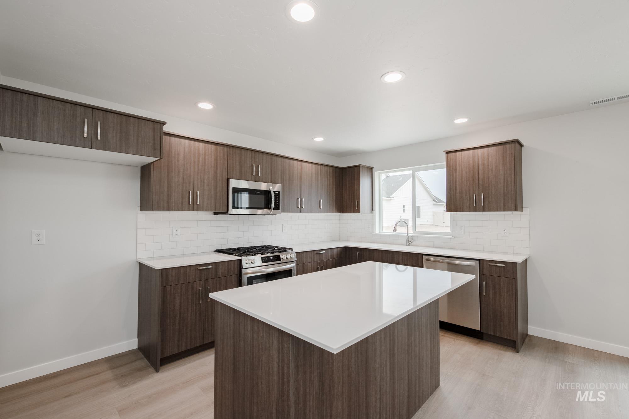 Kitchen featuring backsplash, appliances with stainless steel finishes, dark brown cabinets, light wood-style floors, and a center island