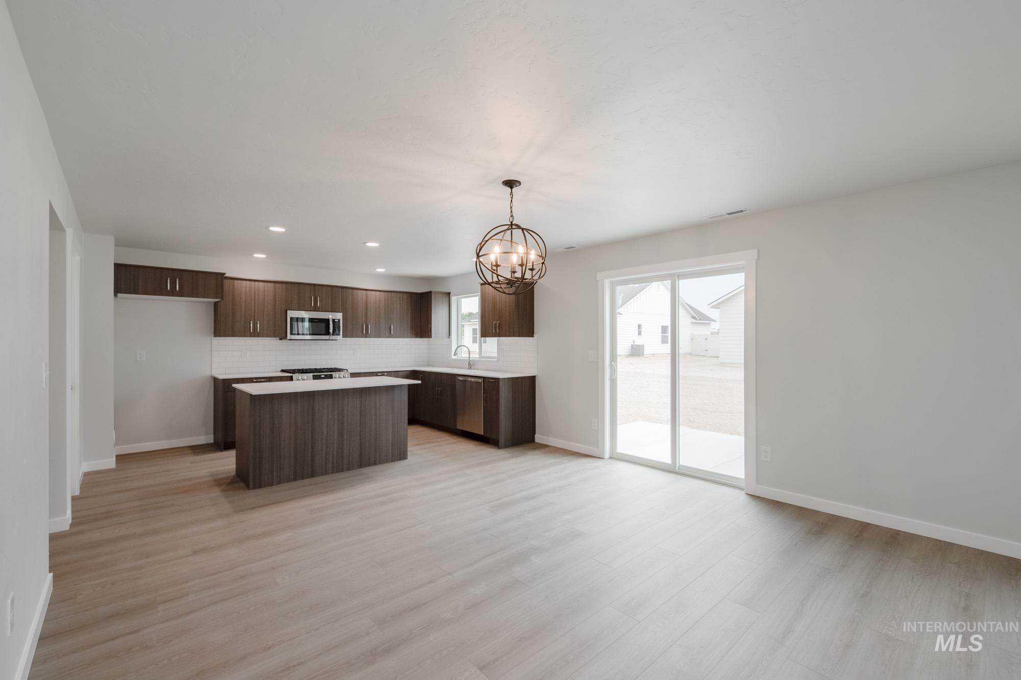 Kitchen featuring hanging light fixtures, light countertops, a kitchen island, dark brown cabinets, and a chandelier