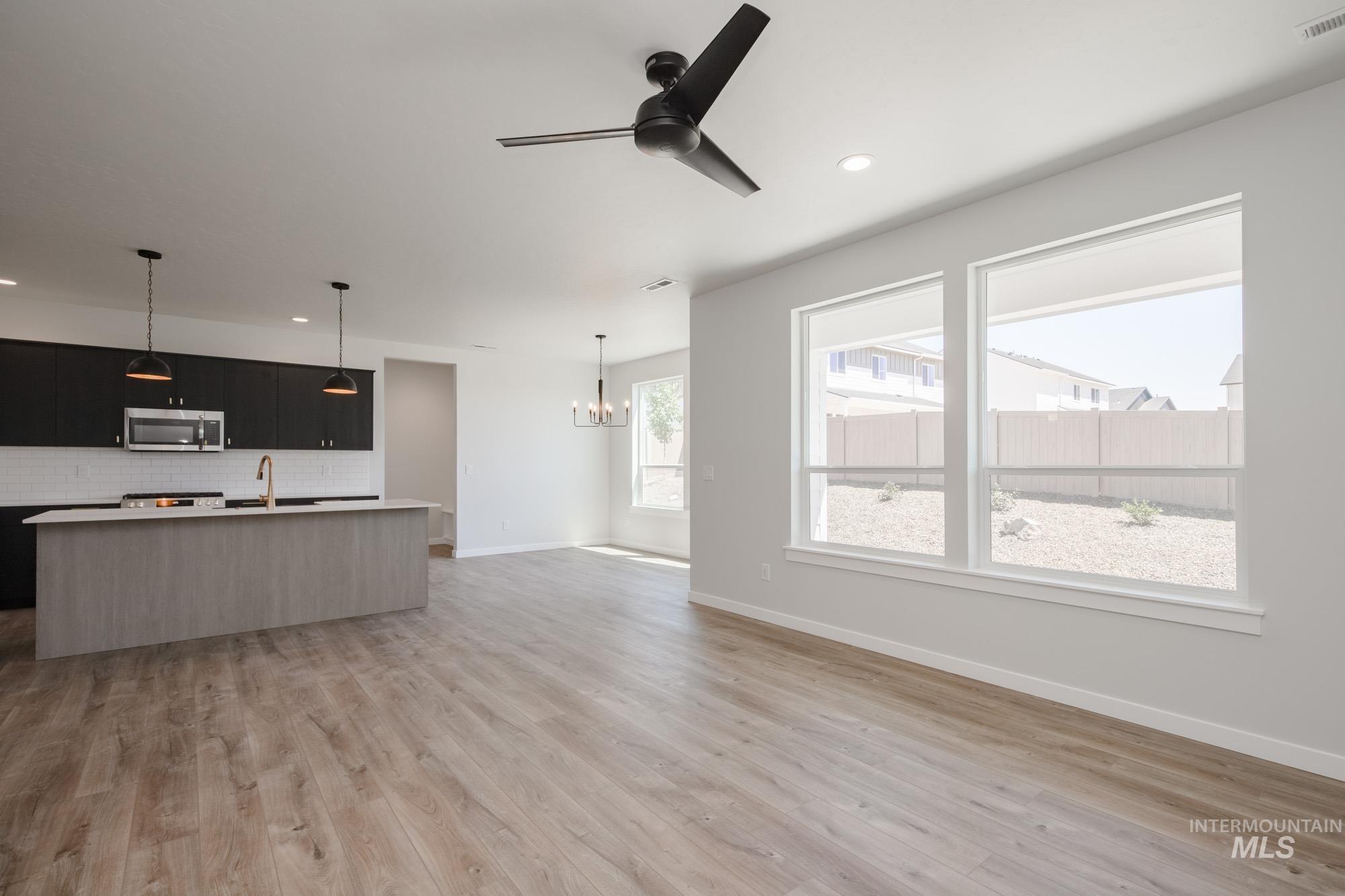 Kitchen with an island with sink, hanging light fixtures, dark cabinets, open floor plan, and tasteful backsplash