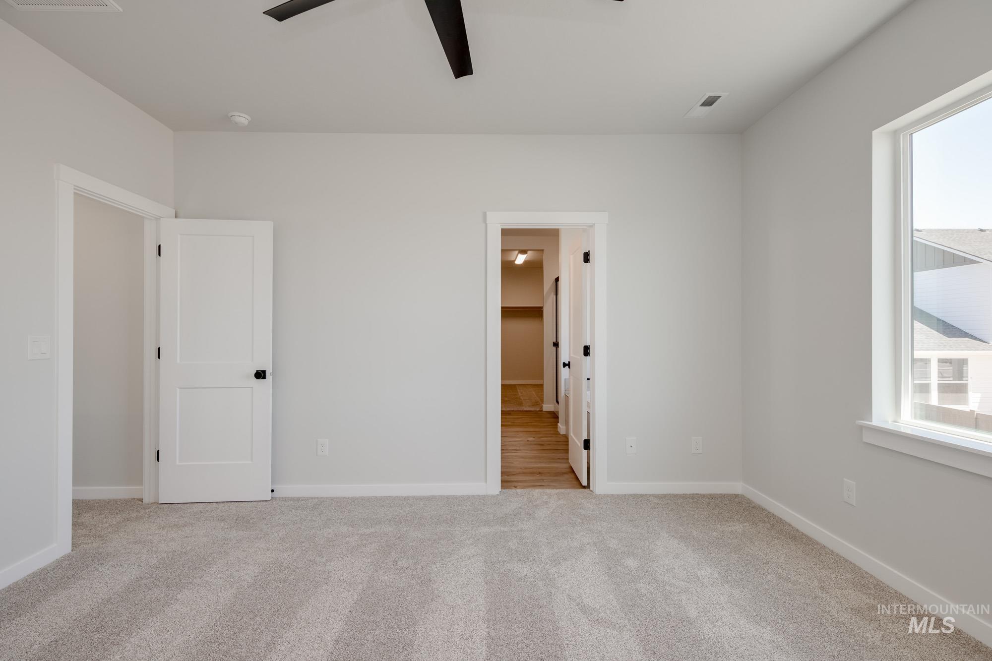 Unfurnished bedroom with light colored carpet, multiple windows, a ceiling fan, and connected bathroom