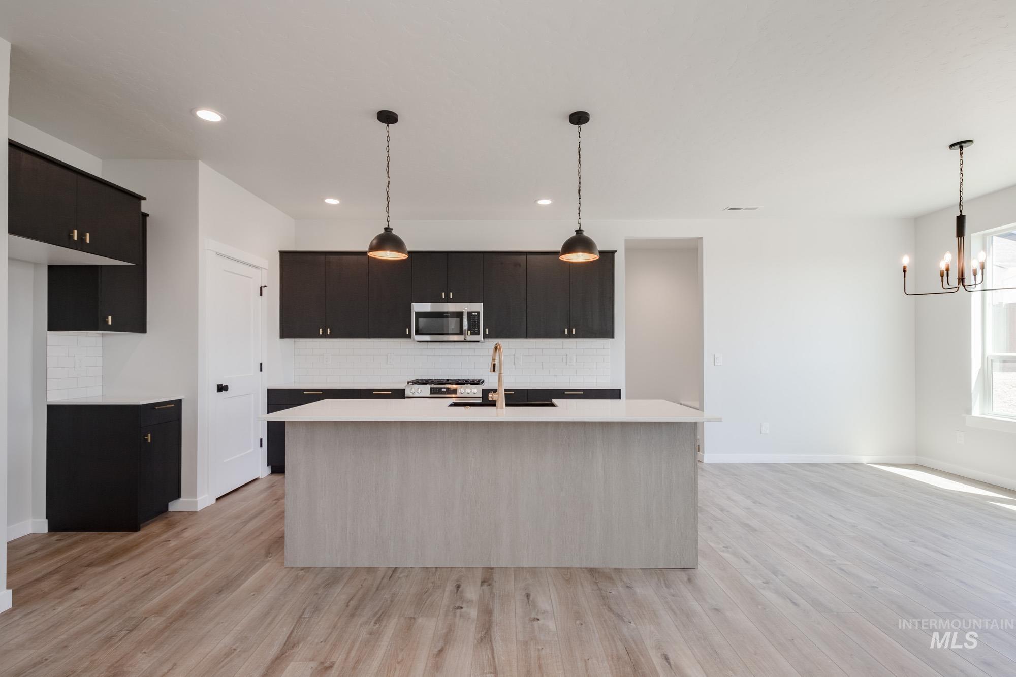 Kitchen featuring decorative light fixtures, decorative backsplash, an island with sink, light wood-style floors, and recessed lighting