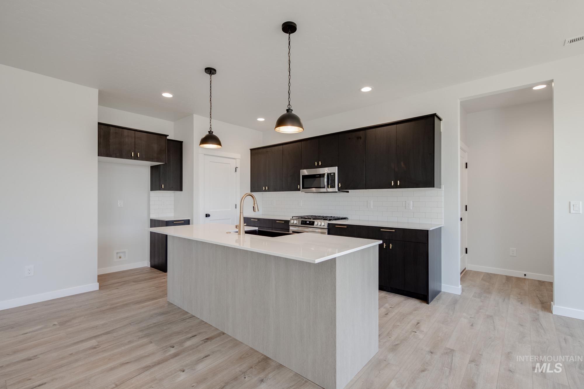 Kitchen featuring tasteful backsplash, hanging light fixtures, a kitchen island with sink, stainless steel appliances, and recessed lighting
