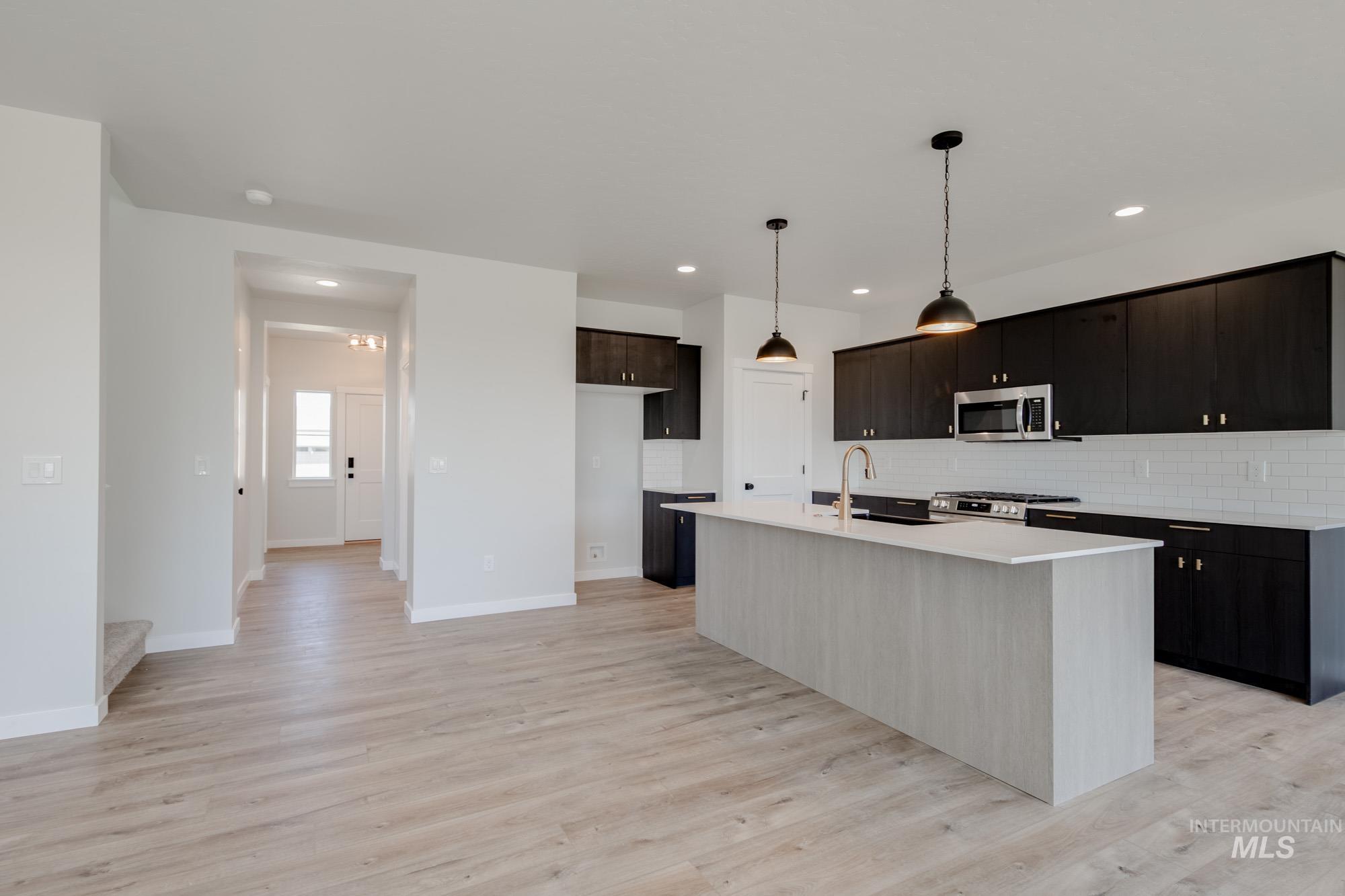 Kitchen with tasteful backsplash, a center island with sink, hanging light fixtures, light wood finished floors, and recessed lighting