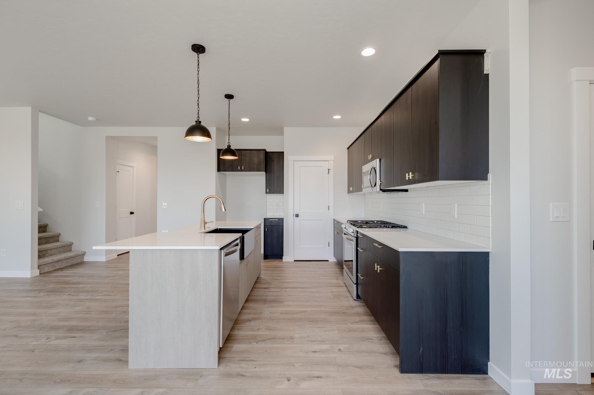 Kitchen with decorative backsplash, appliances with stainless steel finishes, hanging light fixtures, an island with sink, and light wood-type flooring