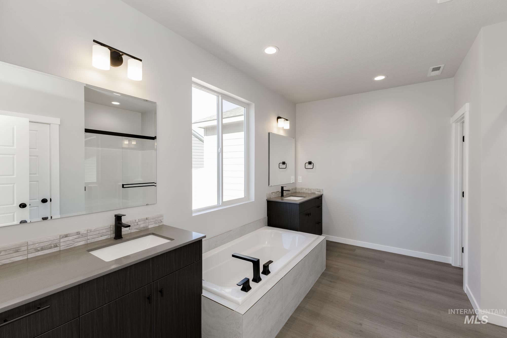Full bath featuring two vanities, a bath, recessed lighting, light wood-type flooring, and a stall shower