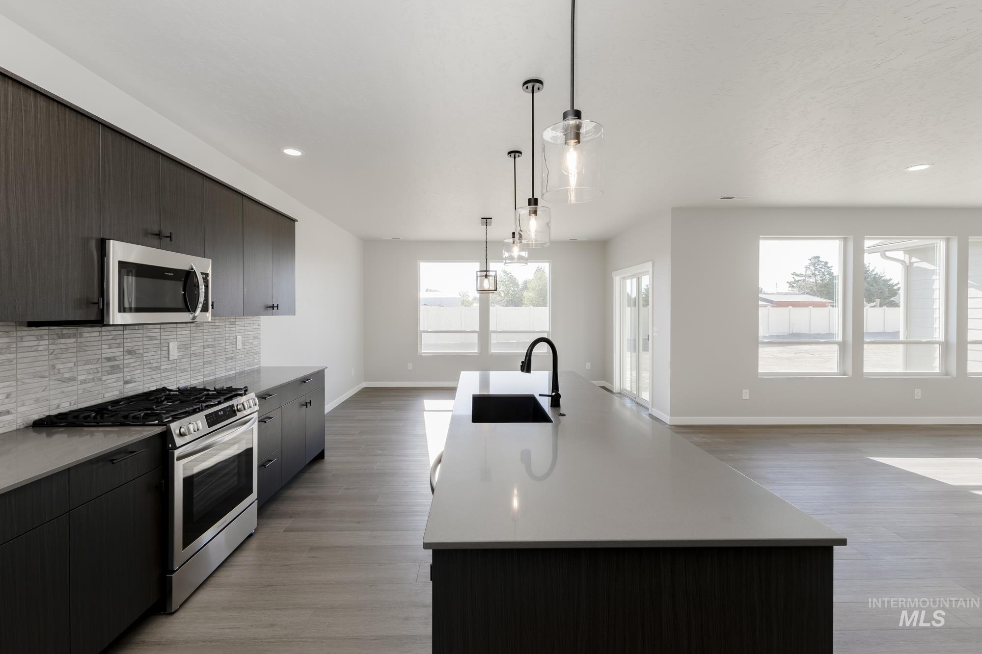 Kitchen with stainless steel appliances, a kitchen island with sink, hanging light fixtures, modern cabinets, and decorative backsplash