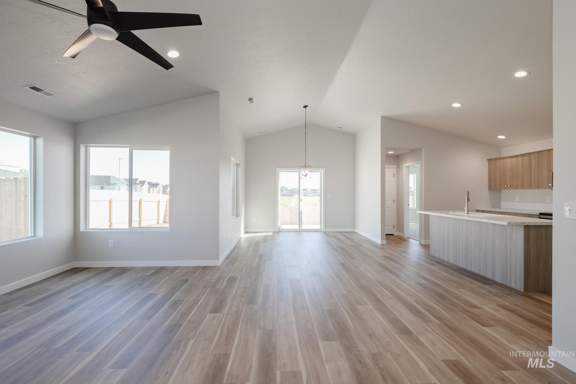 Unfurnished living room featuring ceiling fan, lofted ceiling, light wood finished floors, recessed lighting, and a chandelier