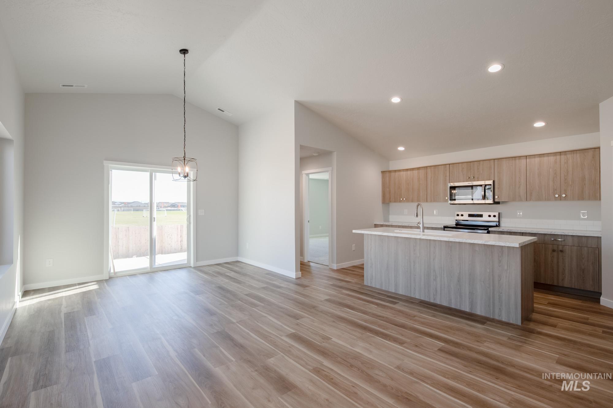 Kitchen with a kitchen island with sink, open floor plan, a chandelier, lofted ceiling, and light wood-style flooring