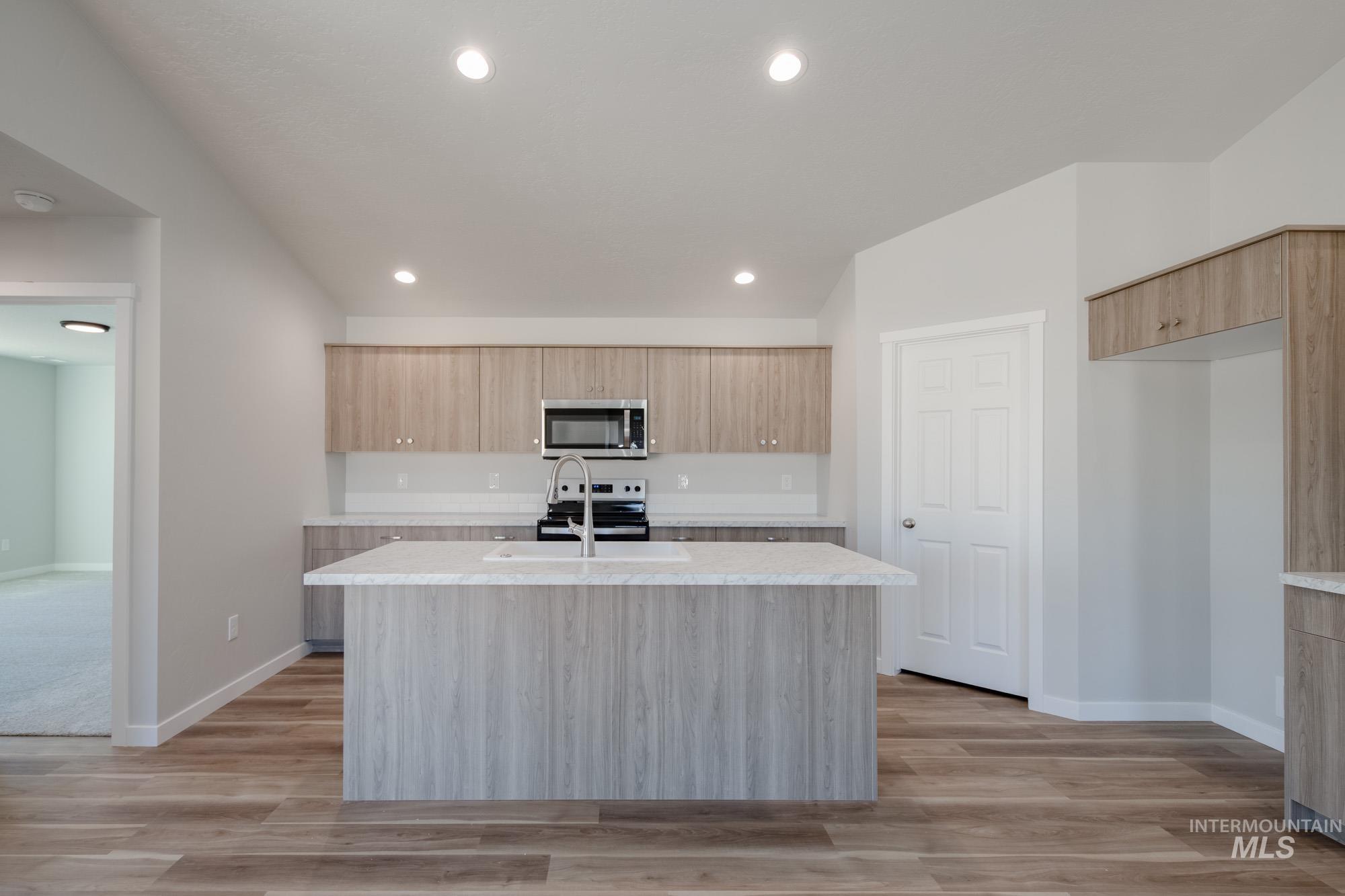 Kitchen with light brown cabinetry, a center island with sink, modern cabinets, appliances with stainless steel finishes, and recessed lighting