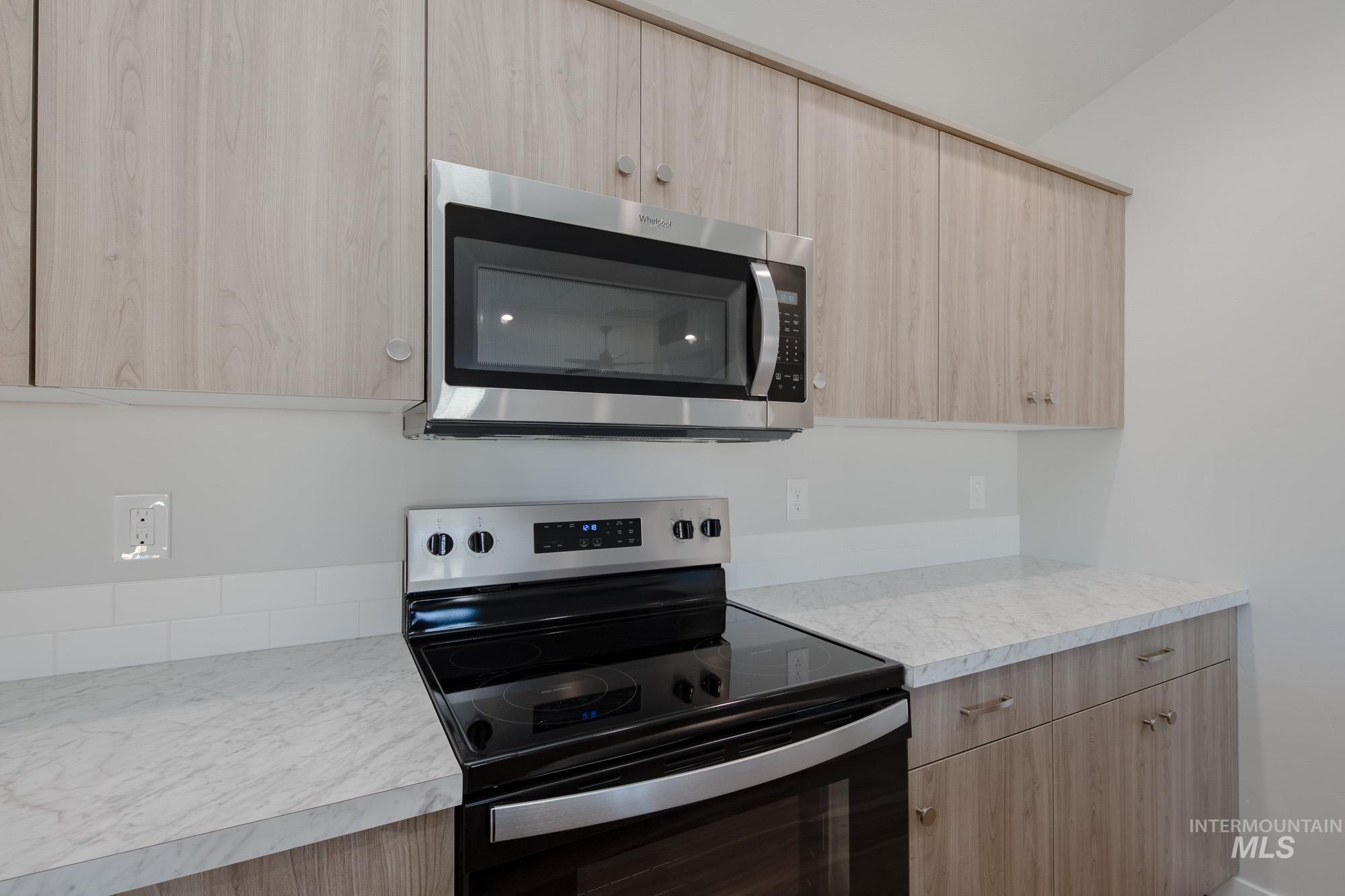 Kitchen with light brown cabinets, electric range oven, stainless steel microwave, light countertops, and modern cabinets