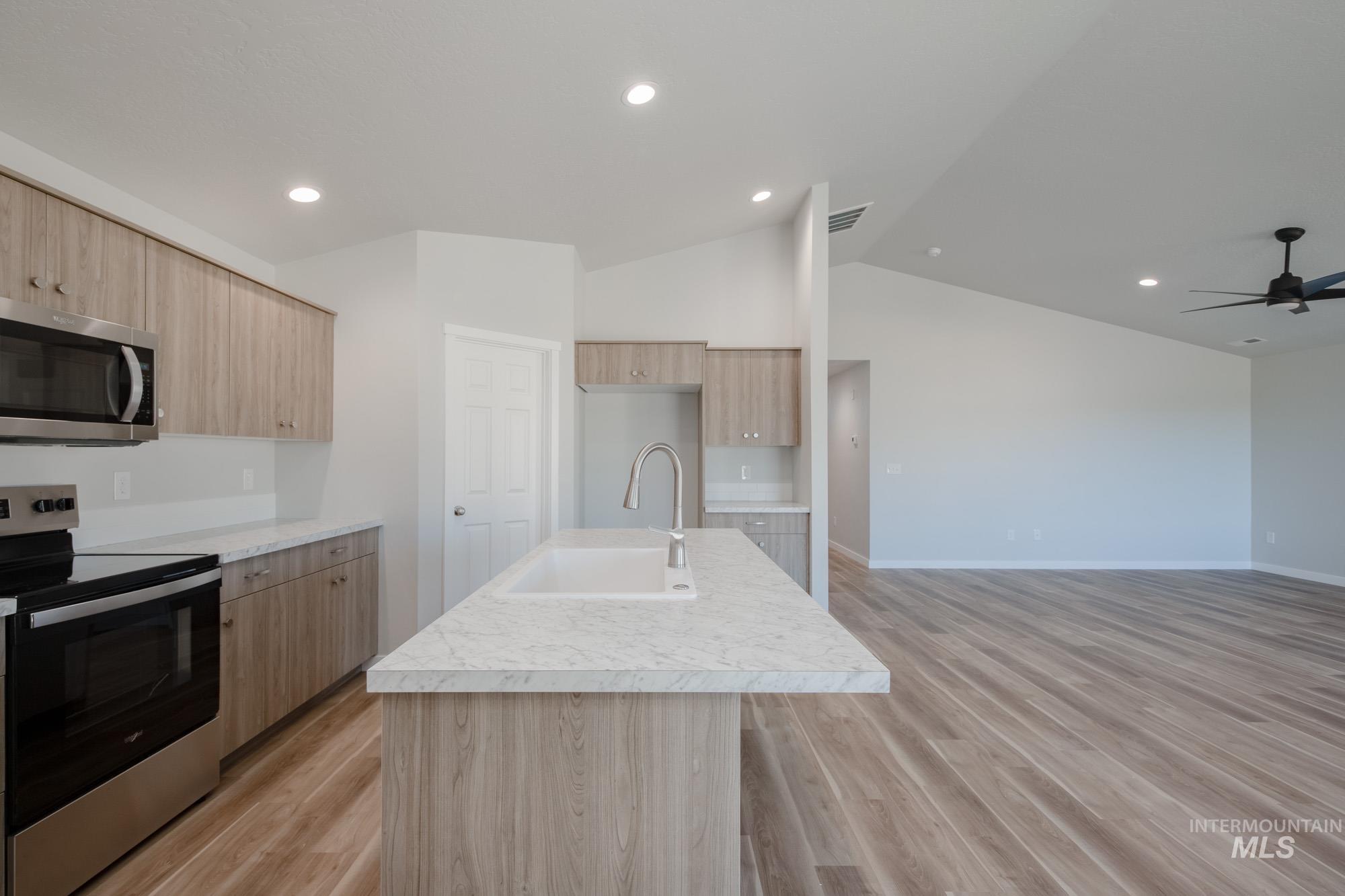 Kitchen featuring stainless steel appliances, light wood-type flooring, lofted ceiling, light countertops, and a kitchen island with sink