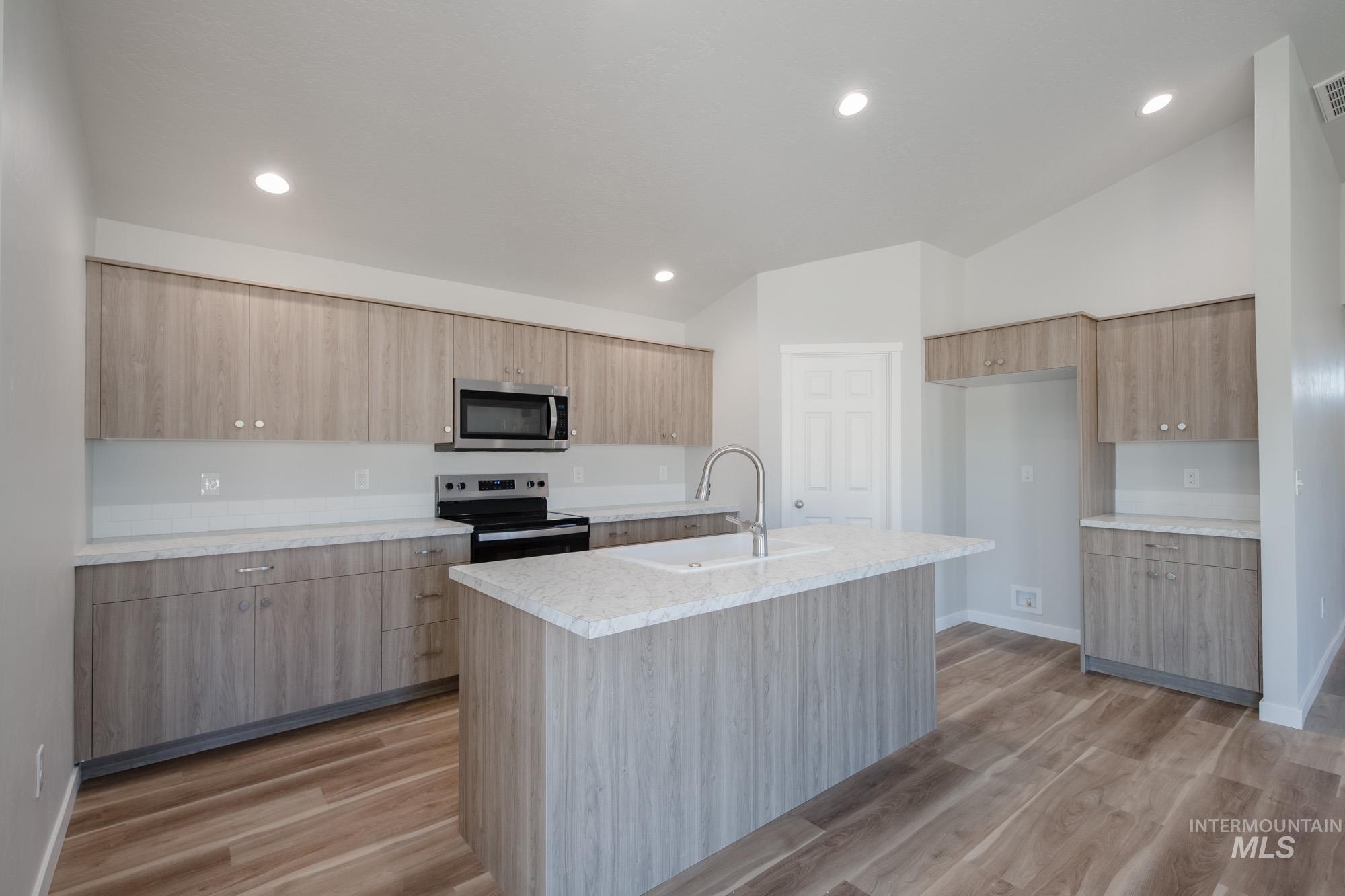 Kitchen with appliances with stainless steel finishes, light wood-type flooring, recessed lighting, modern cabinets, and a center island with sink