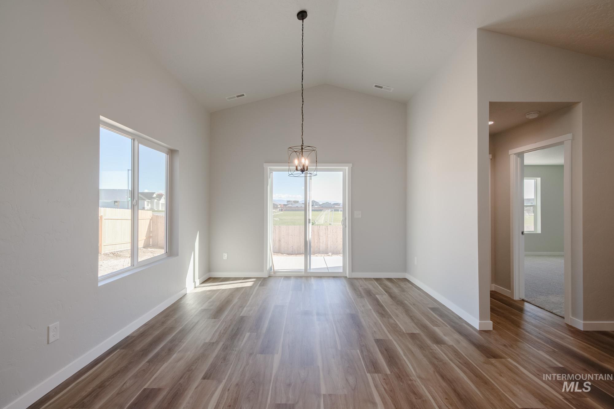Unfurnished dining area with lofted ceiling, healthy amount of natural light, wood finished floors, and a chandelier